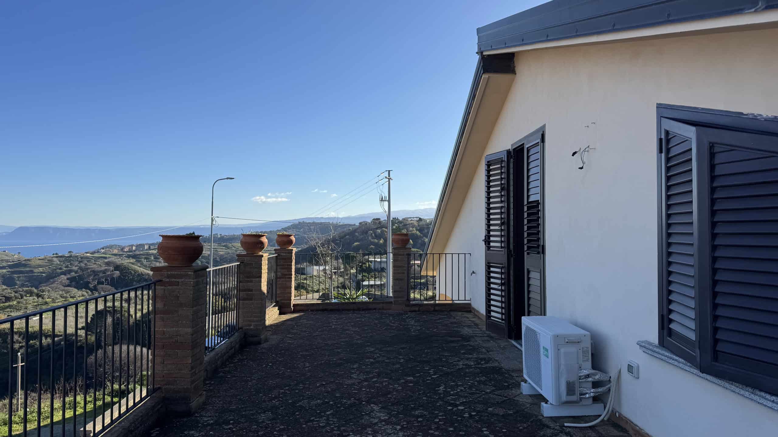Vista panoramica dalla terrazza di casa con fiori in terracotta e paesaggio collinare, ideale per immobili di lusso e case con vista mare, immersi nella natura.
