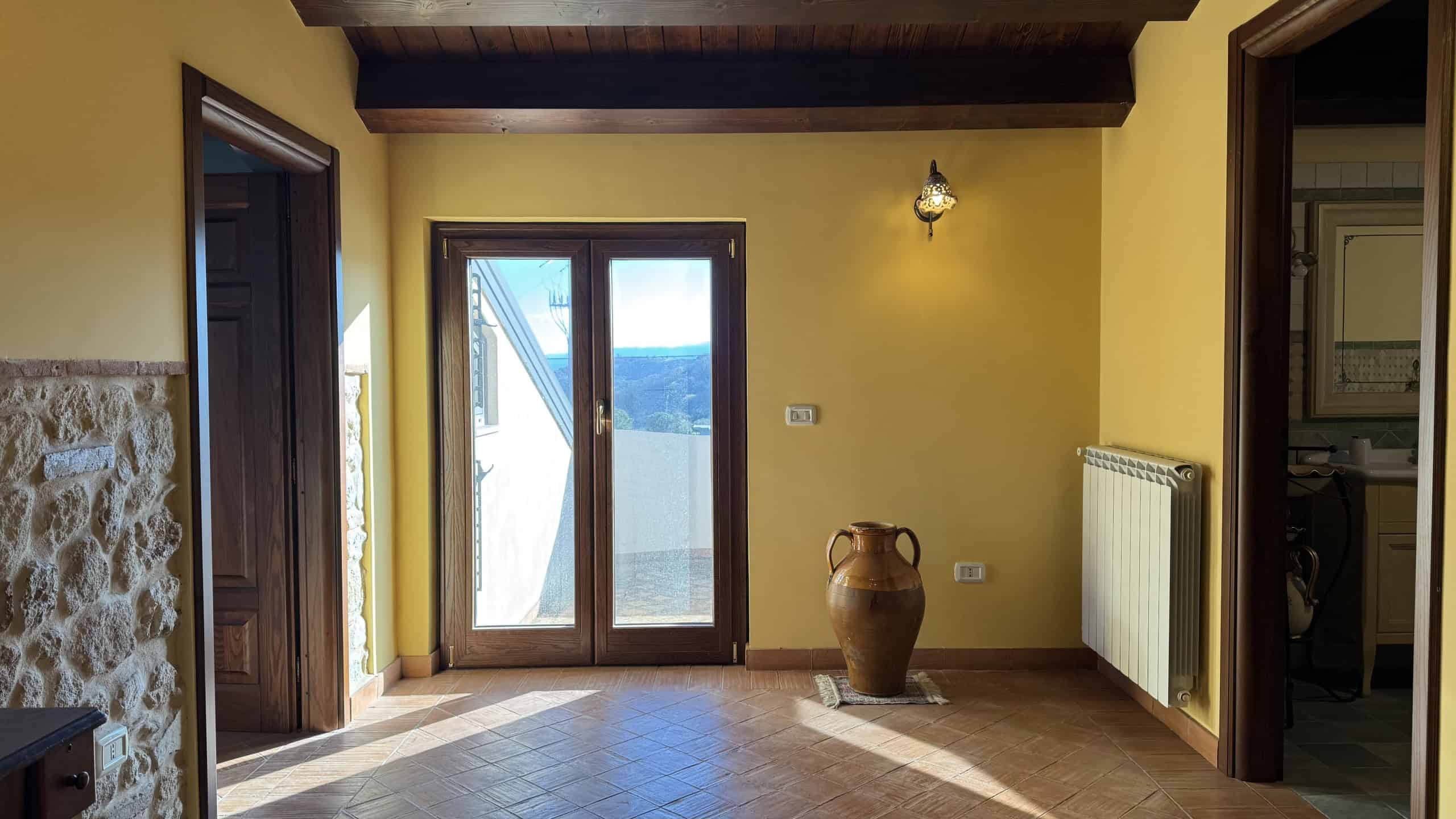Ampio soggiorno con porta finestra panoramica, pareti gialle, dettagli in stile rustico, luminoso e accogliente, perfetto per realizzare un'abitazione di charme.