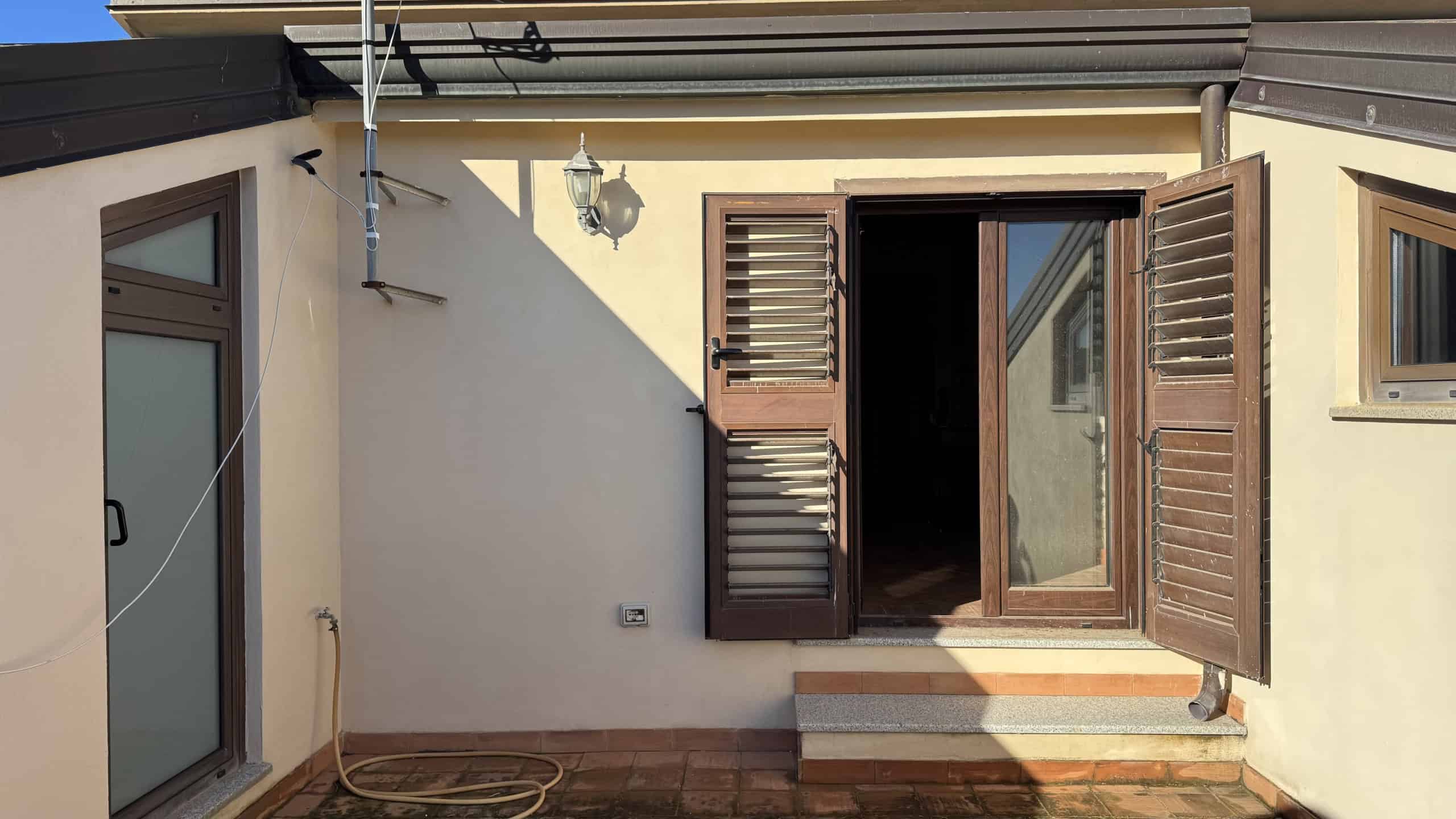 1. Porta finestra in legno con battenti scorrevoli e persiane venete, ideali per case e appartamenti, con spazio esterno in cotto e illuminazione esterna.