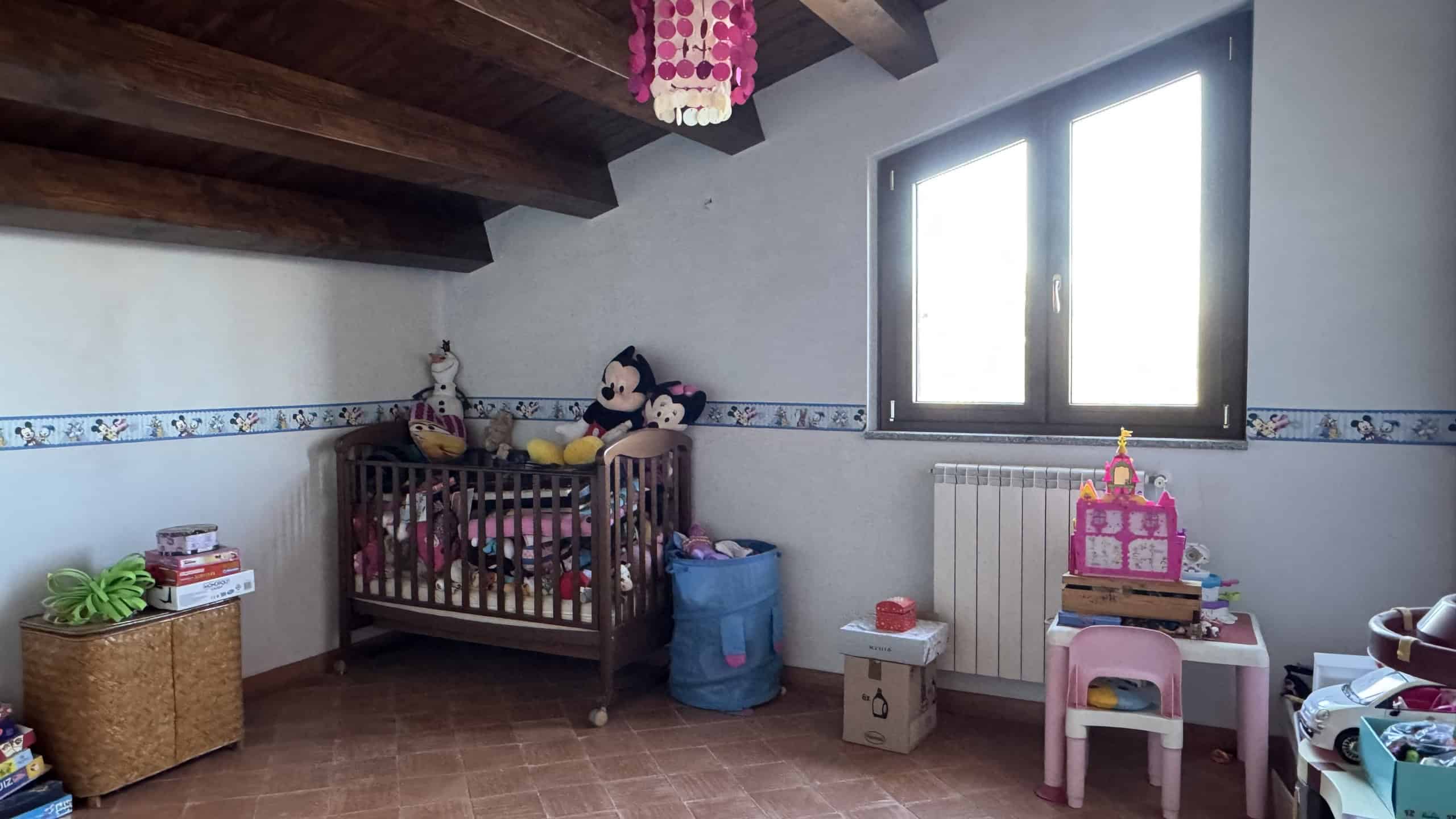 1. Cameretta per bambini con finestra, lettino in legno, giocattoli Disney e decorazioni colorate, ideale per spazi dedicati ai più piccoli.