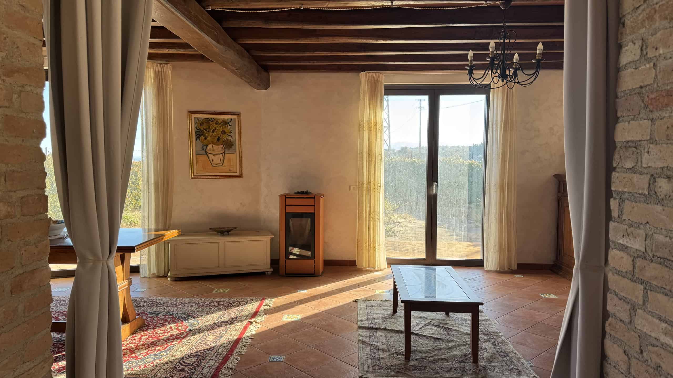 Accogliente soggiorno con mobili in stile rustico, grandi finestre e luce naturale, ideale per vivere momenti di relax e convivialità in una casa in campagna.