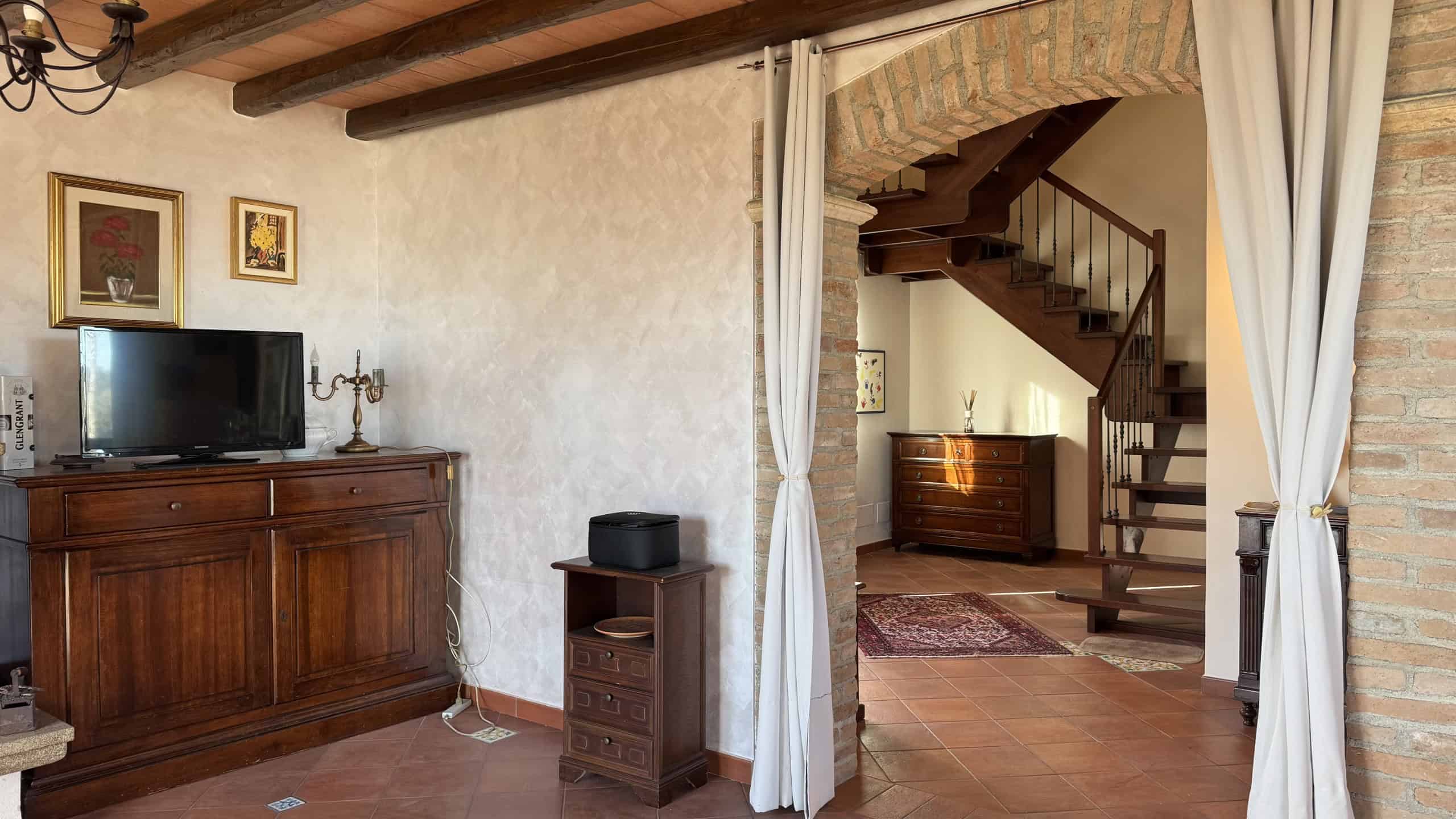 1. Interno soggiorno rustico con mobili in legno, pareti chiare e soffitto con travi in legno, decorazioni classiche e zona TV.