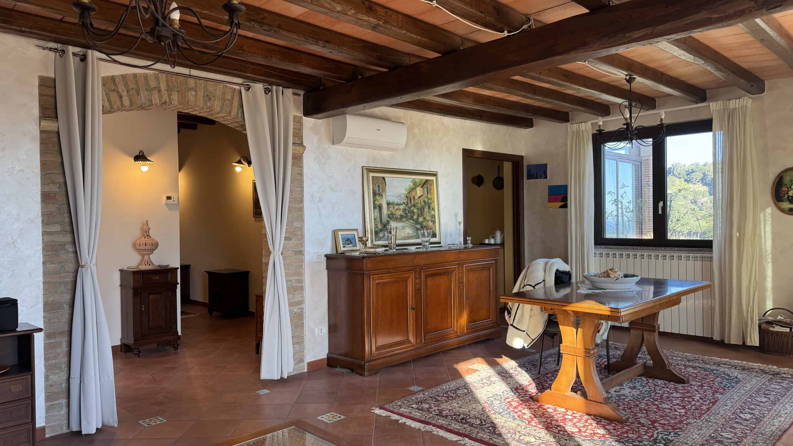 1. Spazioso soggiorno in stile rustico con travi a vista, arredi in legno e lampadario elegante, ideale per vivere momenti di relax e convivialità.