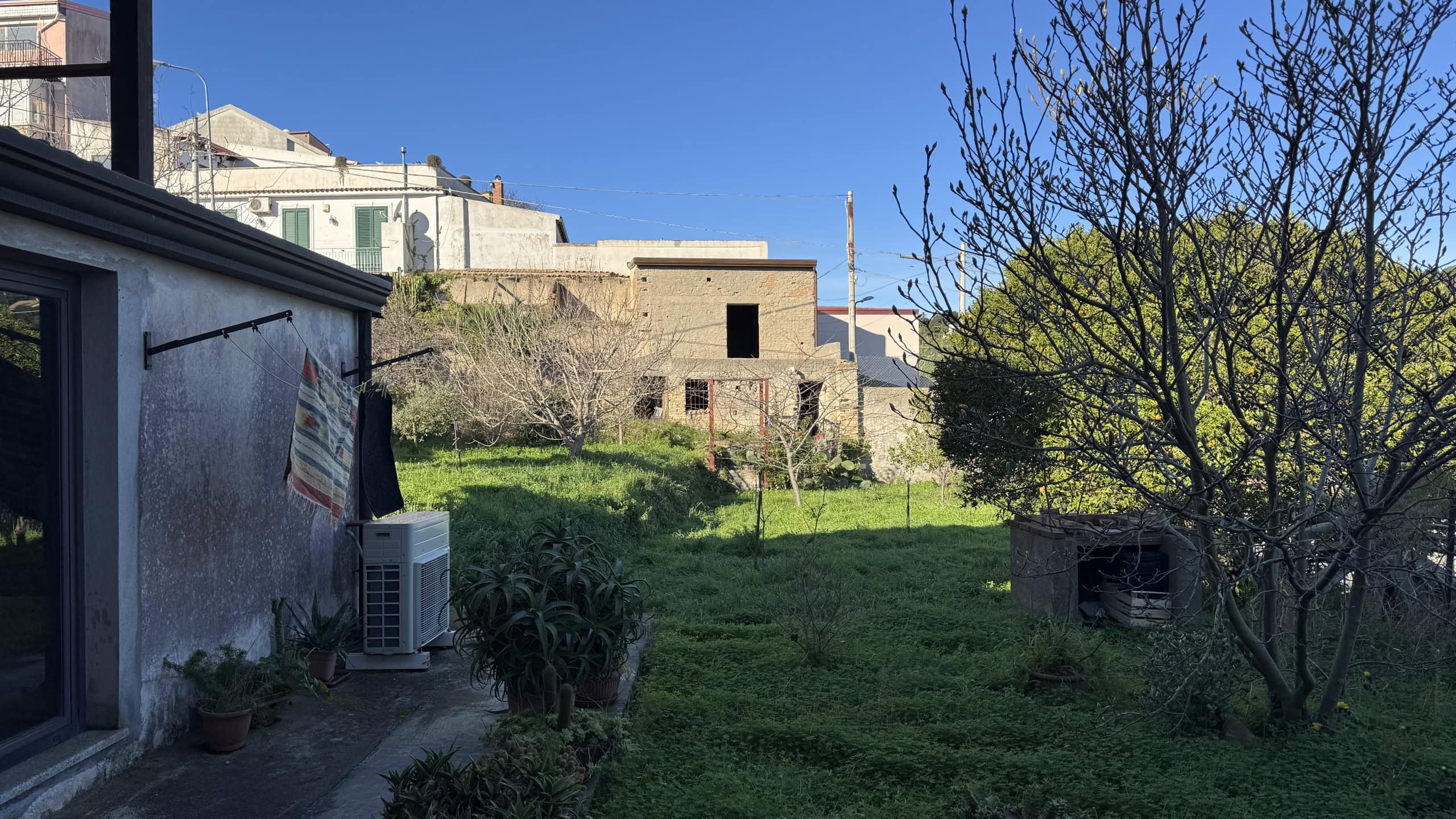 1. Cortile esterno con giardino verde, alberi e edificio in costruzione, vista in pieno giorno con cielo sereno.