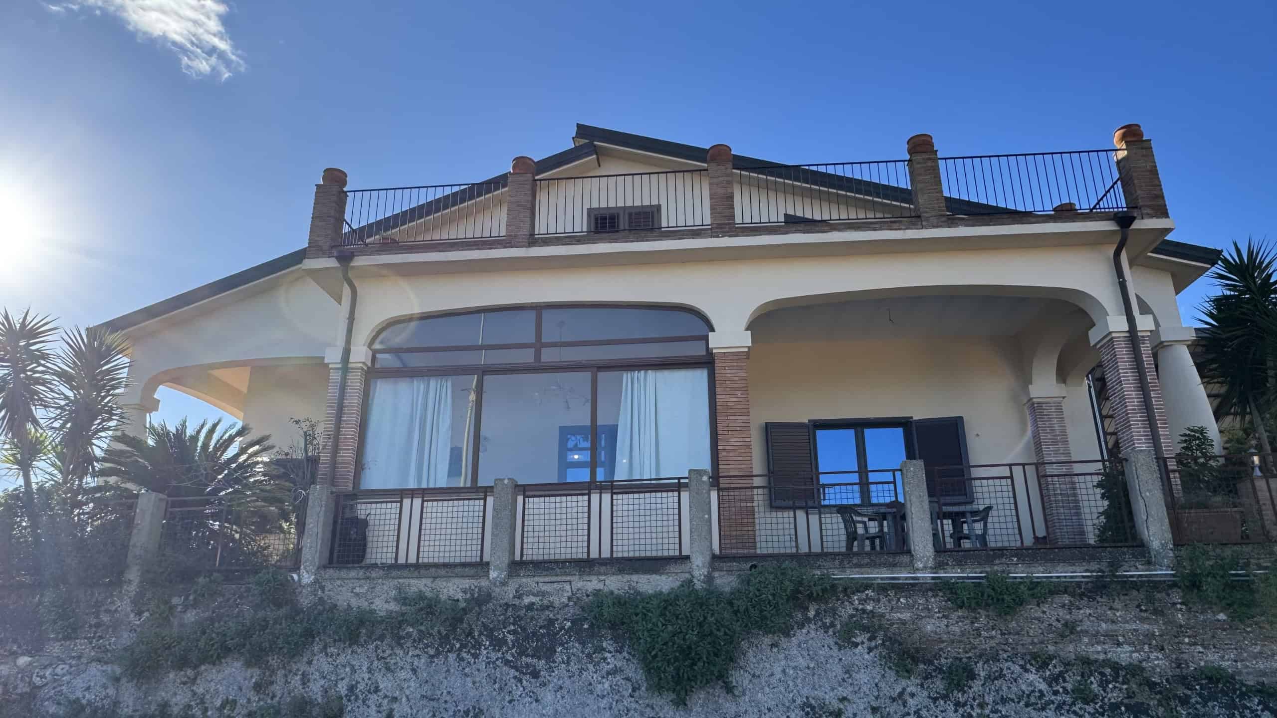 Vista esterna di una villa moderna con ampio balcone e terrazza, perfetta per case di lusso e residenze di prestigio, immersa nel verde con materiali di alta qualità.