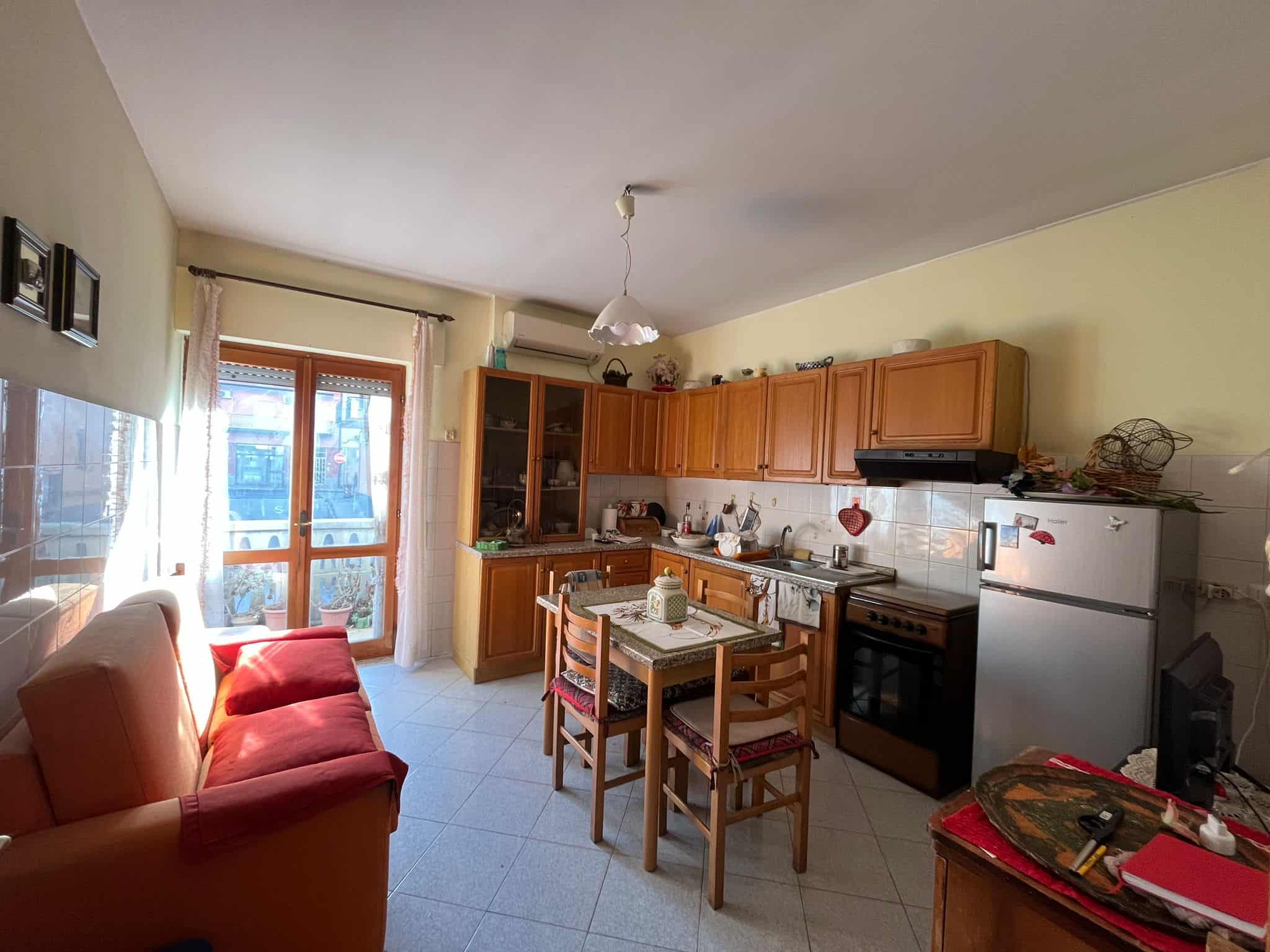 Mobili cucina in legno, tavolo da pranzo e balcone con finestre a doppia anta, atmosfera accogliente.