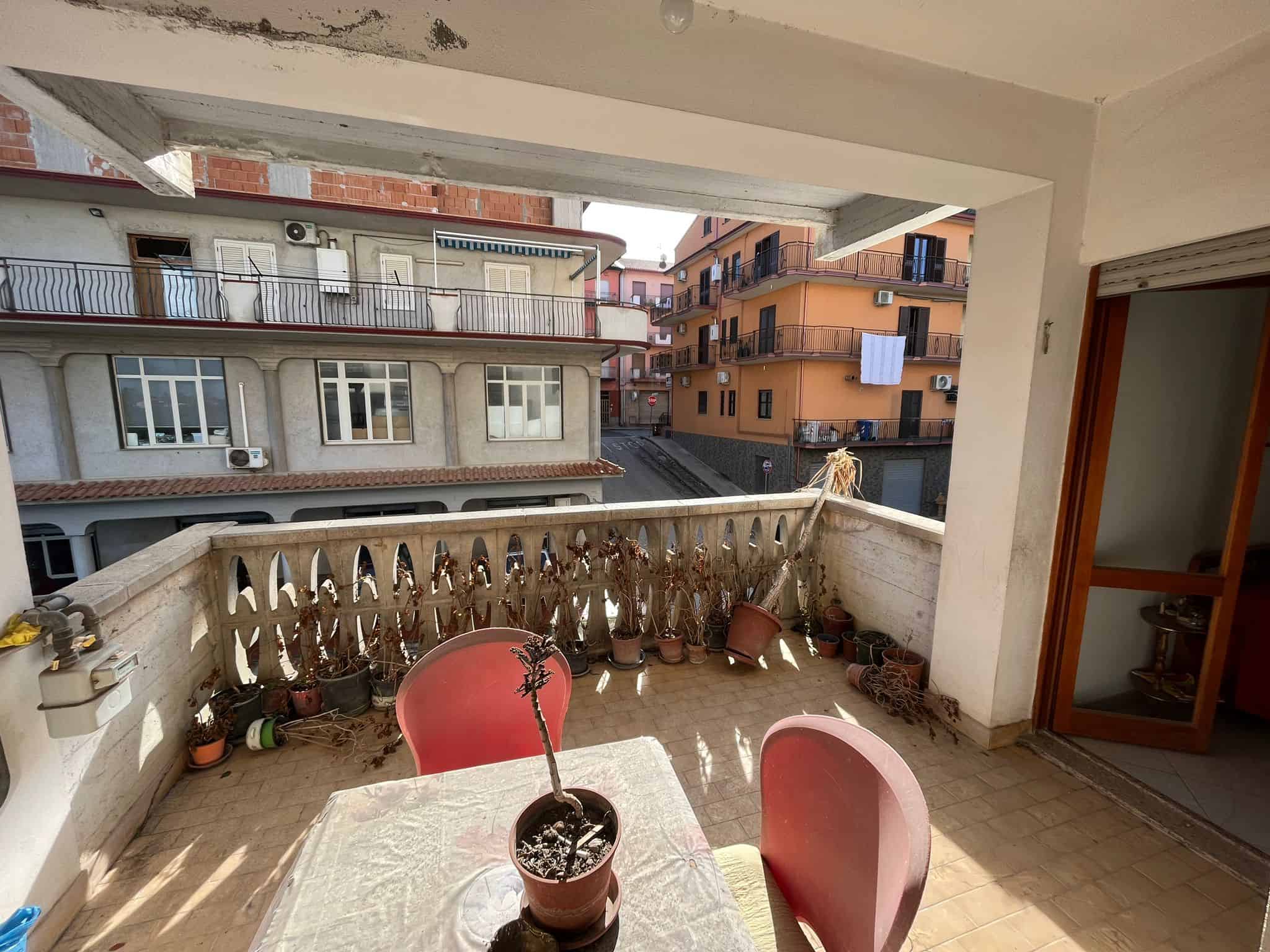 Balcone con piante secche e vista su palazzi residenziali in zona urbana, spazio esterno di appartamento in vendita o affitto in città, ambientazione di vita quotidiana, immagini di immobili NextCasa.