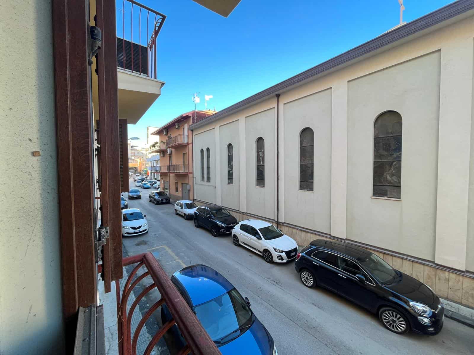 Auto in sosta lungo una strada urbana con edifici residenziali, vista da una finestra, in un giorno soleggiato, immagine chiara e dettagliata, rappresenta un contesto cittadino.