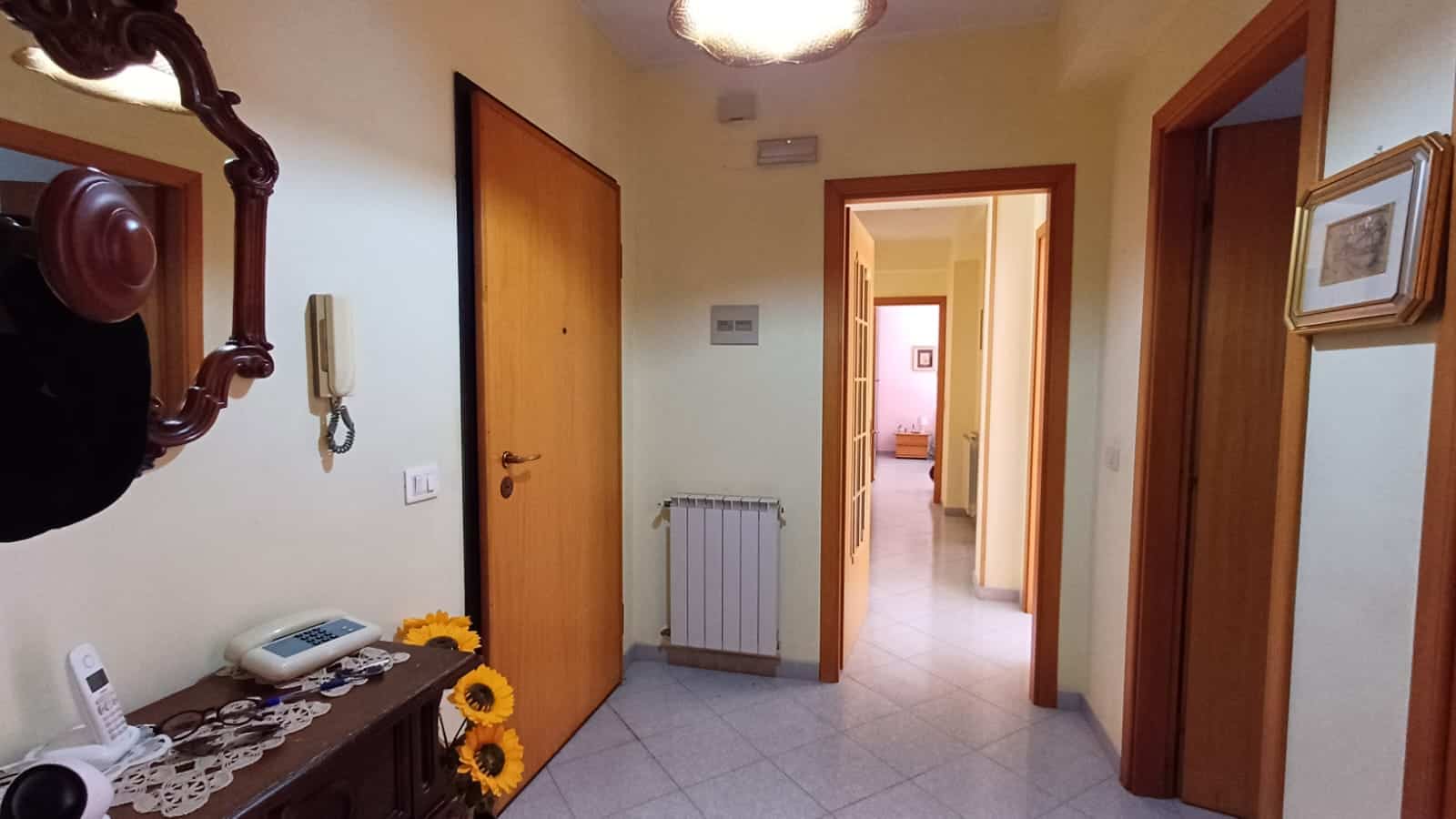 1. Zona ingresso casa con porte in legno, specchio decorativo, telefono, e decorazioni di girasole.