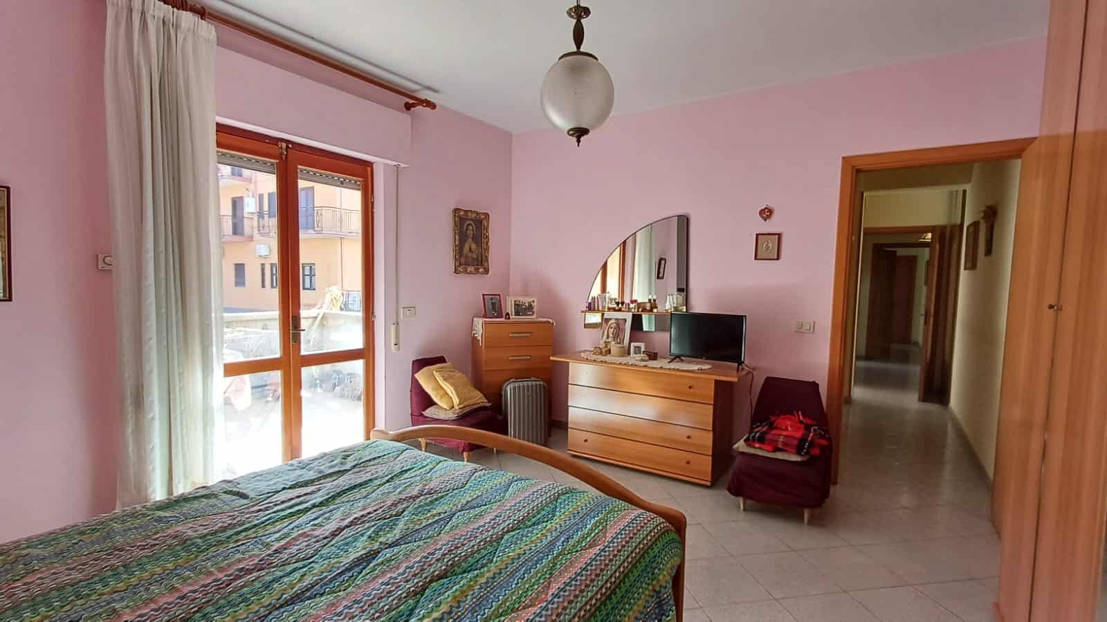 1. Camera da letto funzionale con mobili in legno, finestra con tende e vista su cortile interno, arredamento accogliente e luminoso.