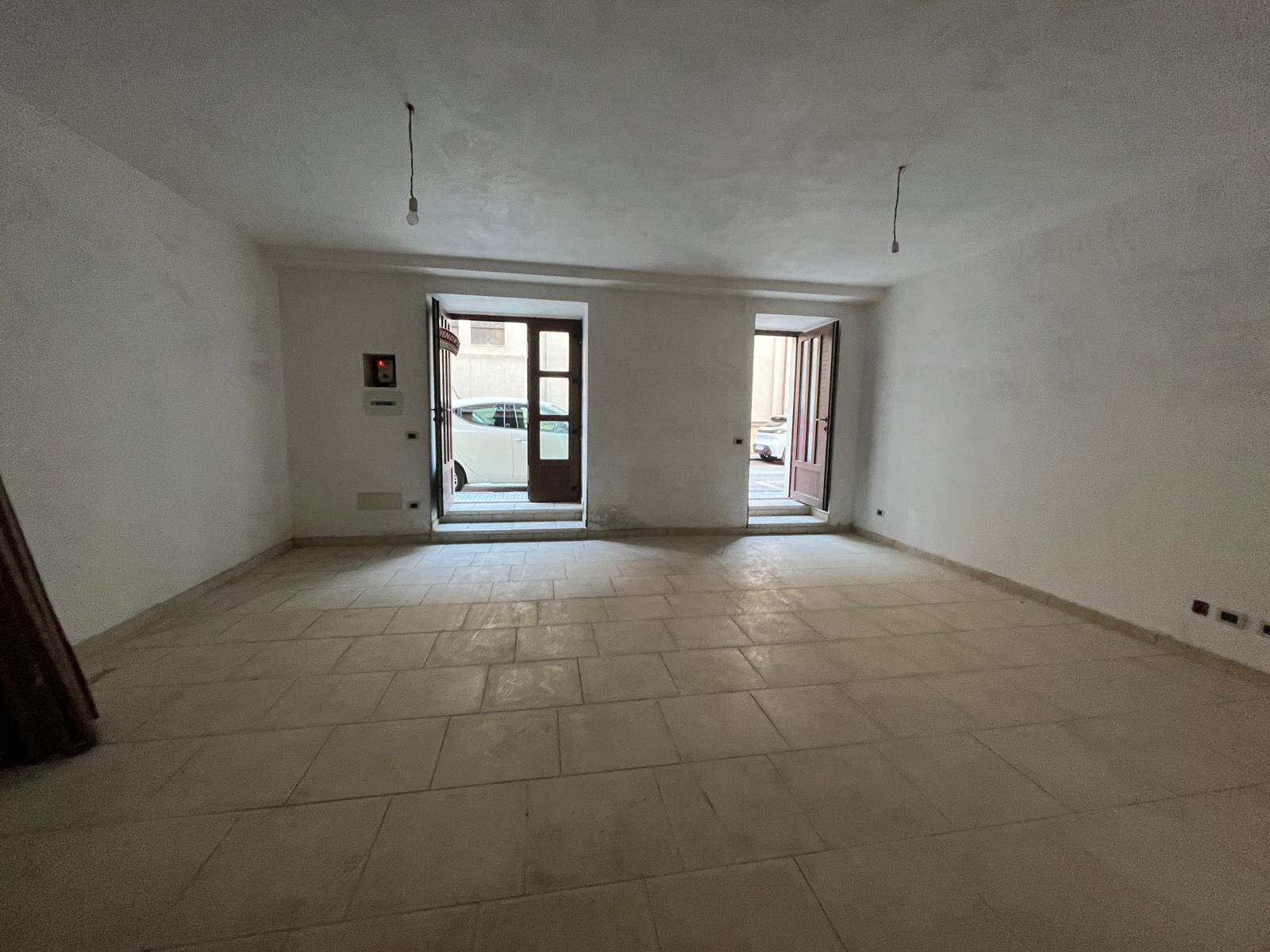 Ampia stanza vuota in fase di ristrutturazione, con pareti bianche e pavimento in piastrelle beige, pronta per essere personalizzata e arredato. Ideale per creare il soggiorno o l'ufficio dei tuoi sog.