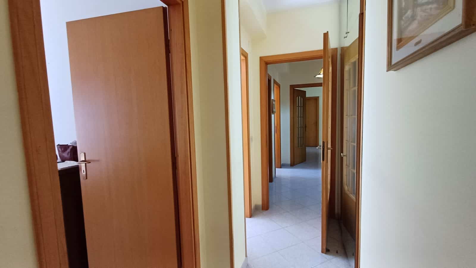 Porta d'ingresso in legno naturale in un appartamento con pareti beige e pavimento piastrellato, ideale per soluzioni di immobili residenziali e case in affitto.