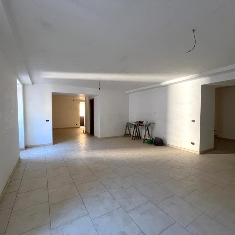 Ampia zona soggiorno in fase di ristrutturazione, luminosa e spaziosa, con pareti bianche e pavimento in gres porcellanato chiaro, pronta per arredi moderni e personalizzazione.