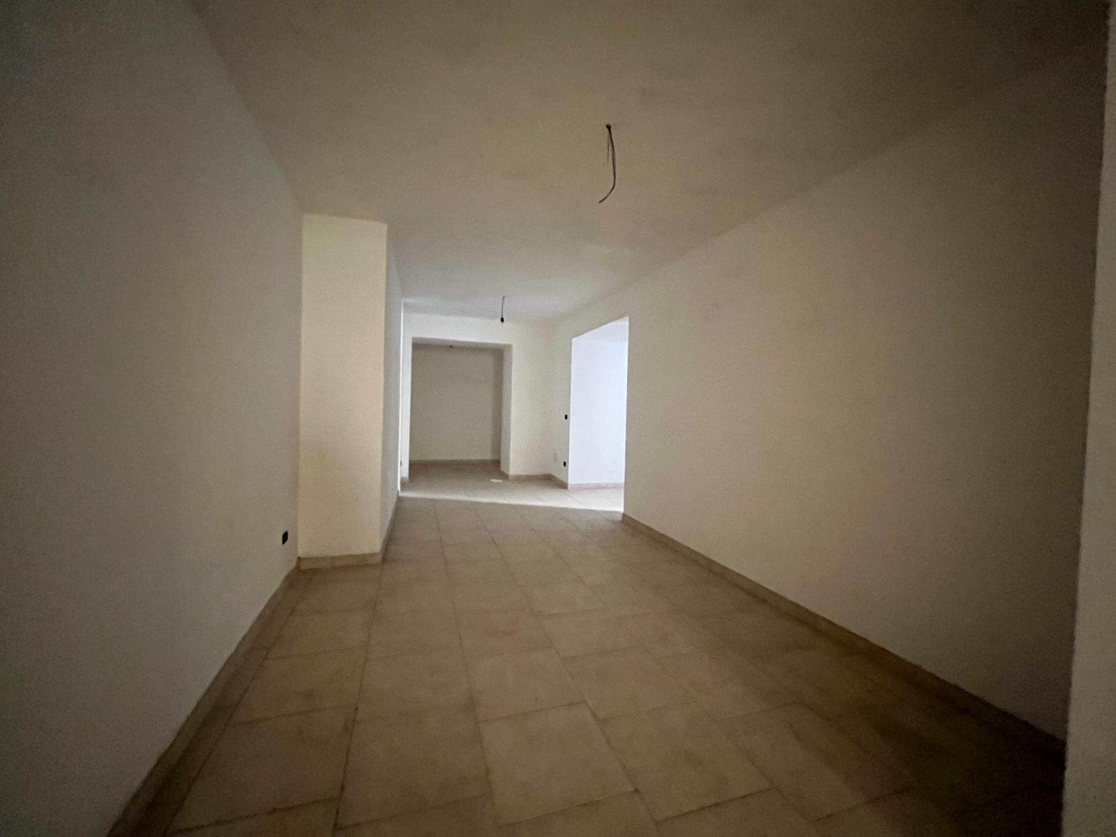 Ampia stanza vuota in fase di ristrutturazione, con pareti bianche e pavimento in piastrelle beige, pronta per essere personalizzata e arredato. Ideale per creare un soggiorno o un ufficio luminoso e.