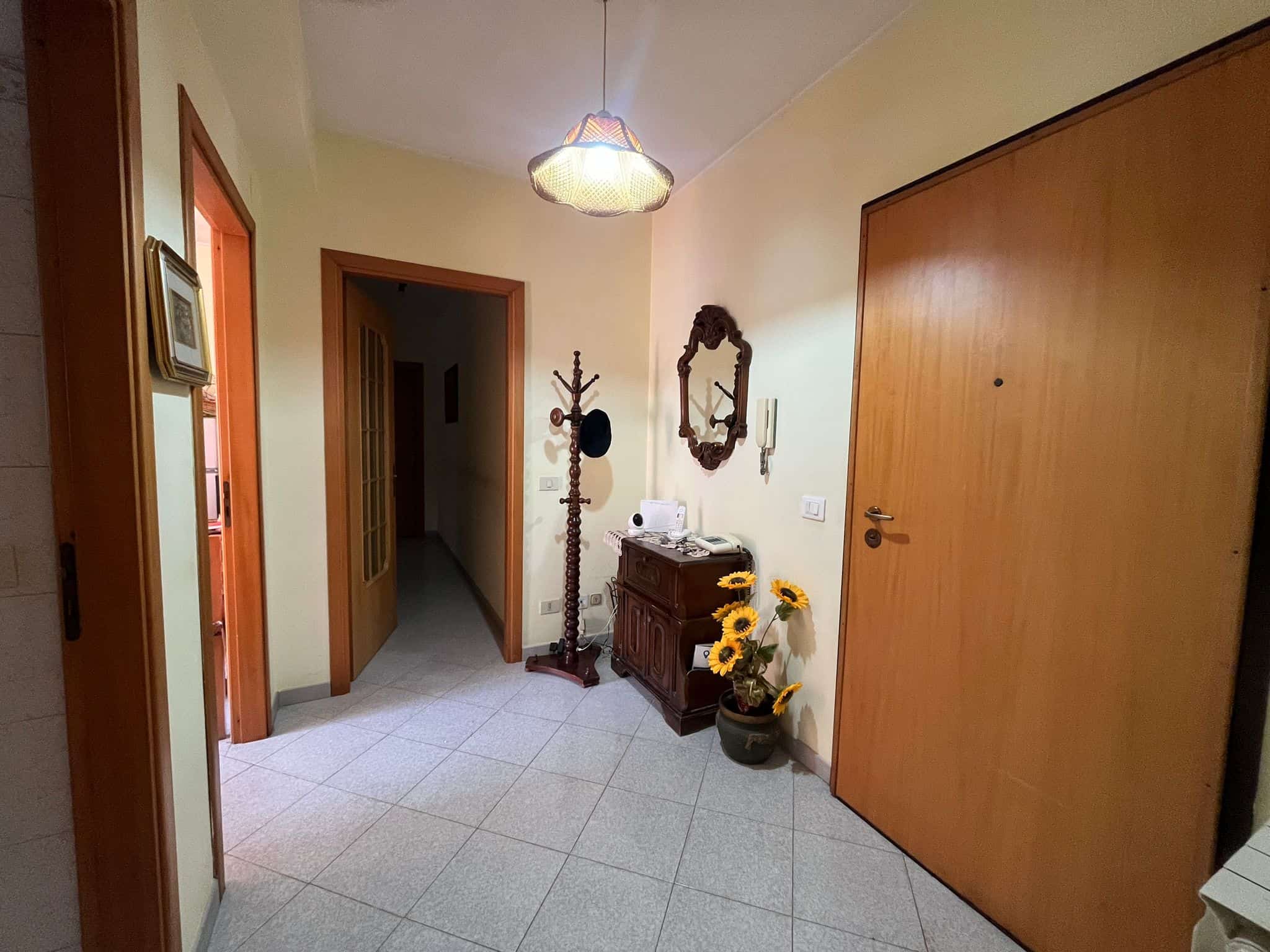 1. Corridoio di casa con porta in legno, specchio vintage e decorazioni floreali, ambiente accogliente e luminoso.