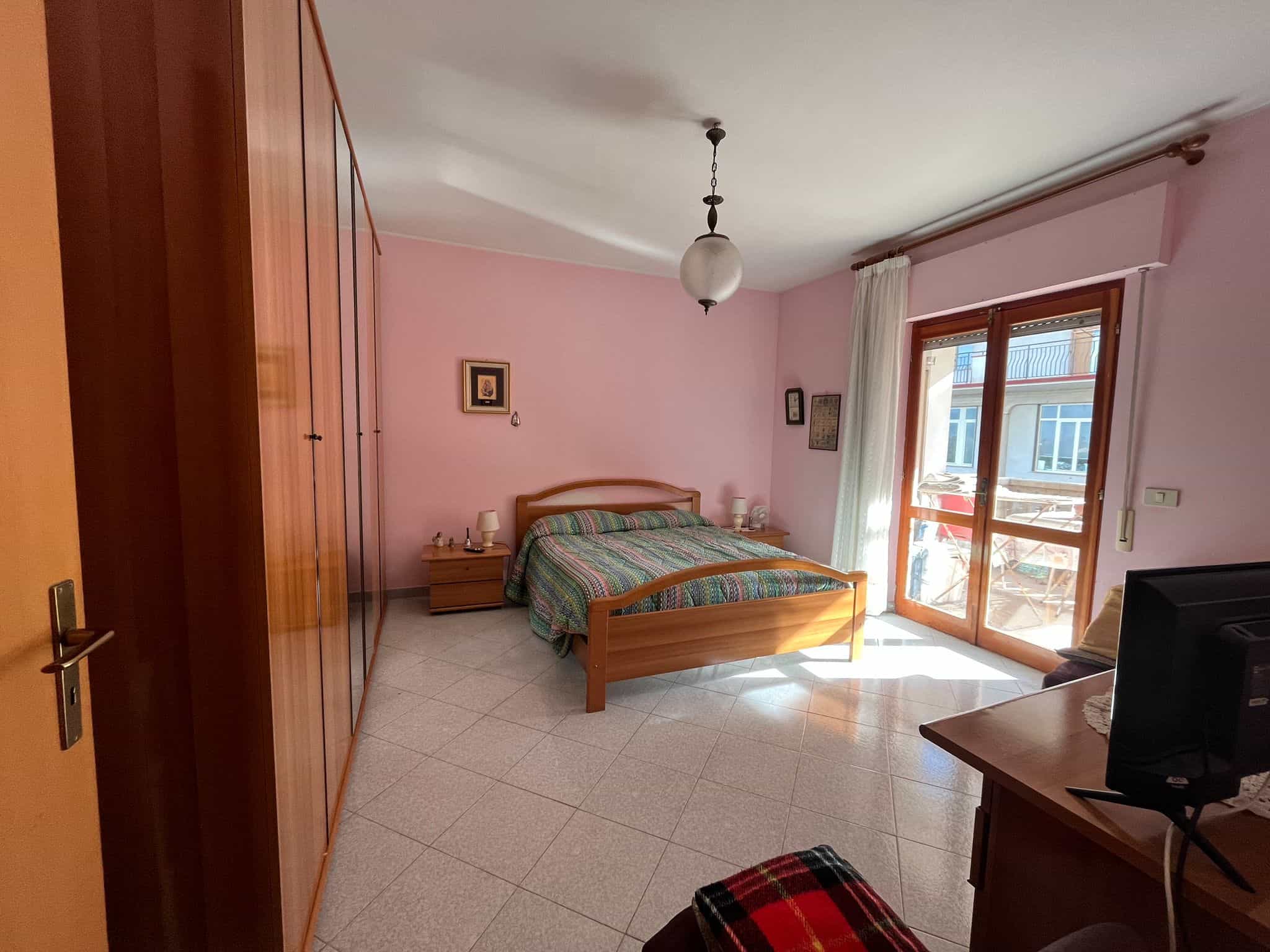 Armadio a muro in legno, camera da letto con finestra grande, arredamento funzionale, ambiente luminoso e accogliente, ideale per appartamenti in vendita o in affitto, stile classico e caldo.