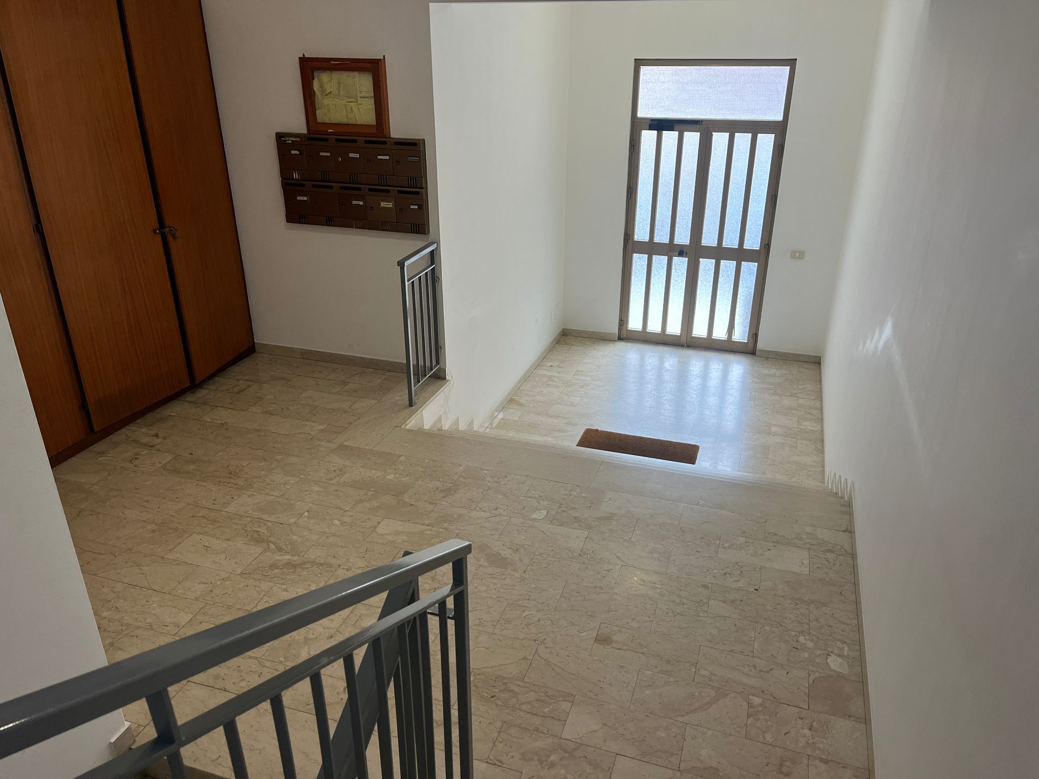 Ampio ingresso con porta finestra, marmo chiaro, armadio a muro e cassette postali, ambiente luminoso, ideale per la vendita immobiliare NextCasa, ottimizzato per ricerca appartamenti e case.