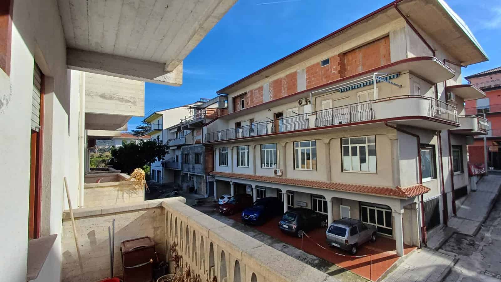 Vista di un edificio residenziale in costruzione con balconi eleganti, mentre le auto sono parcheggiate sotto, nel quartiere di NextCasa, perfetto per investimenti immobiliari a Napoli.