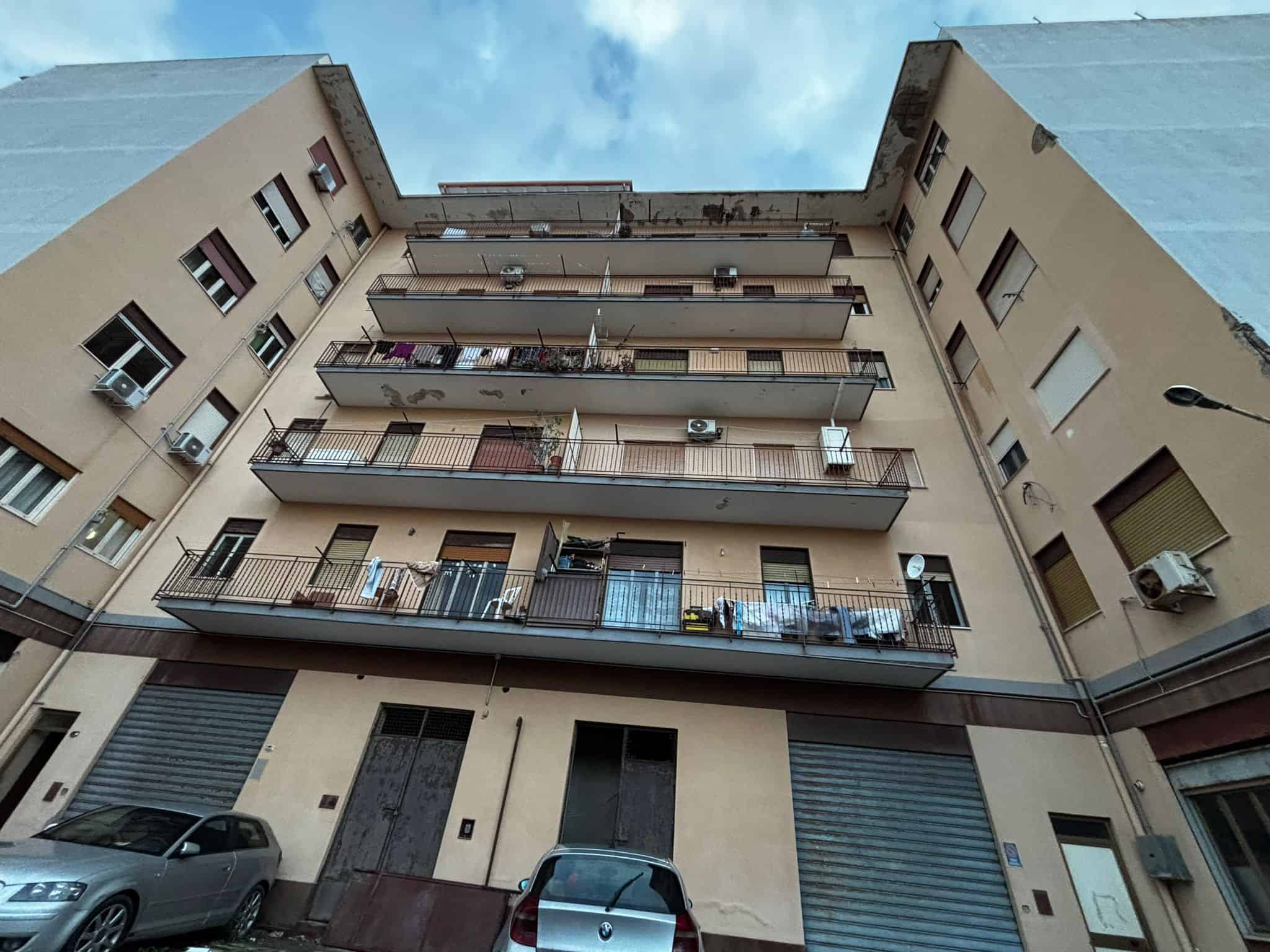 Immagine di un edificio residenziale con balconi e finestre, situato in un contesto urbano. La foto mostra la facciata di un condominio con dettagli architettonici e elementi di vita quotidiana.