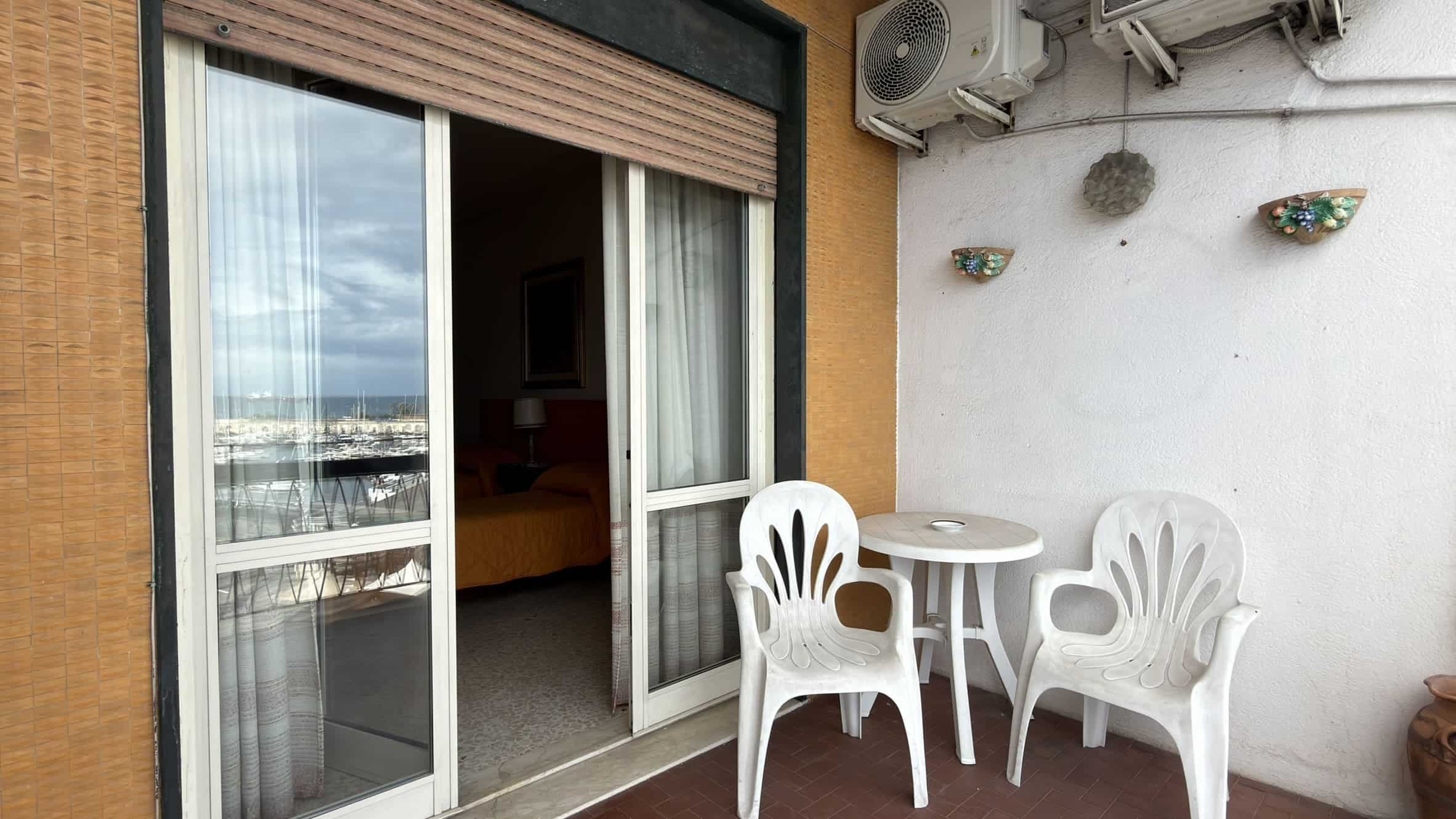 Balcone con sedie e tavolino in plastica bianca, vista su città e cielo, ambiente esterno di un appartamento in stile moderno, ideale per relax e convivialità.