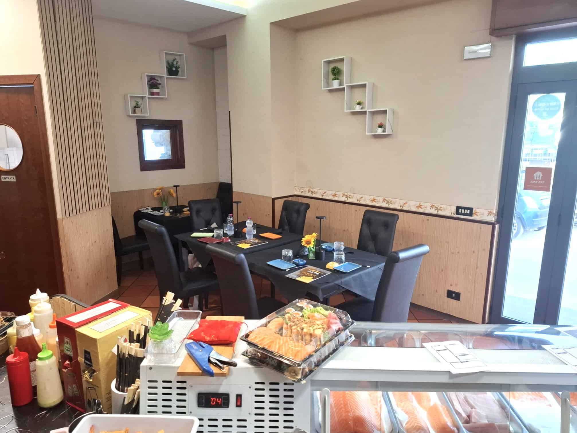 Tavolo da pranzo elegante in un ristorante con sedie nere, decorazioni moderne e pareti beige, pronto per accogliere clienti. Atmosfera accogliente e raffinata ideale per cene e incontri conviviali.