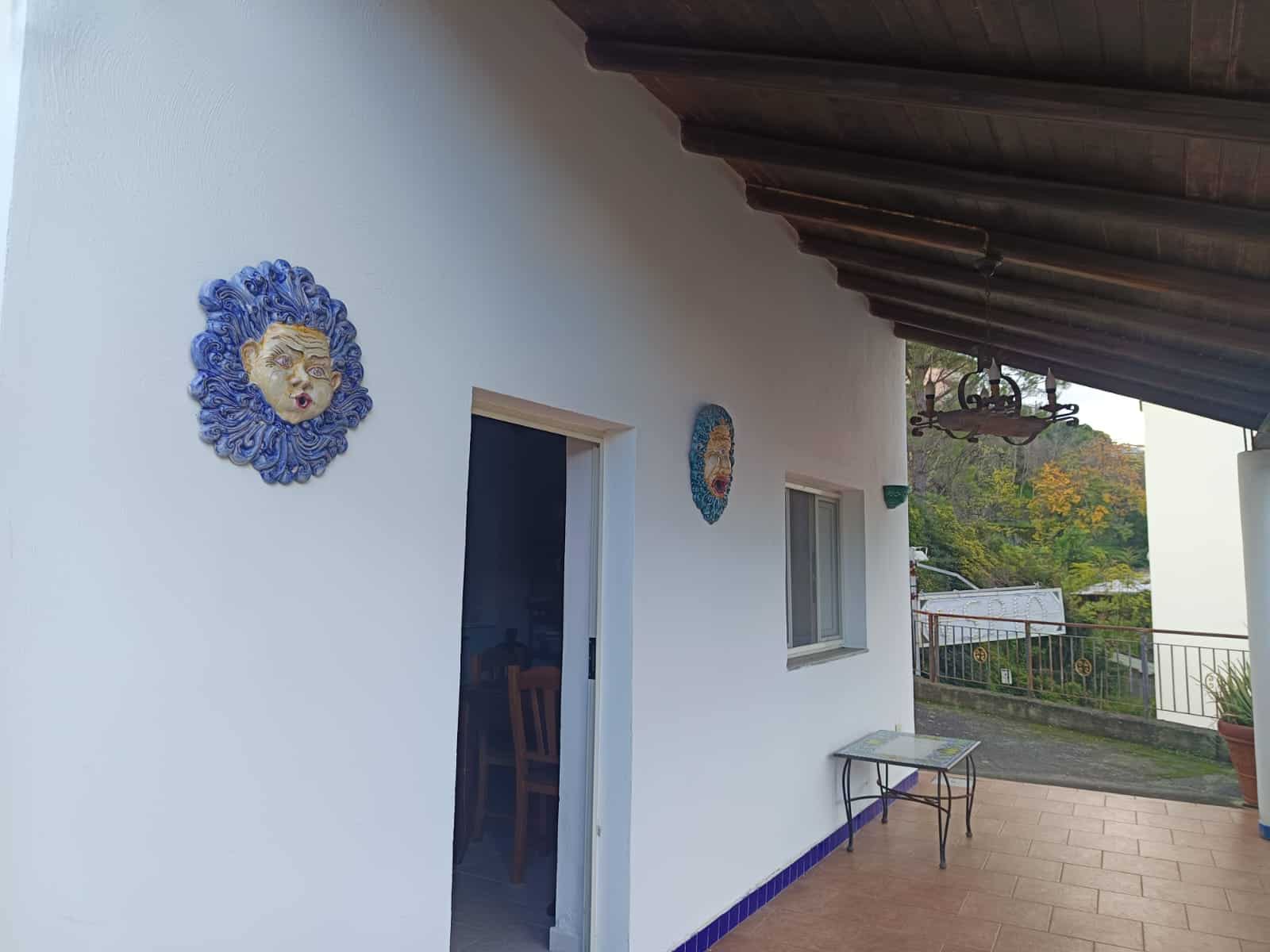 Esterno di una casa con decorazioni artistiche sulla parete bianca, vista su un balcone con vista panoramica sulla natura circostante.