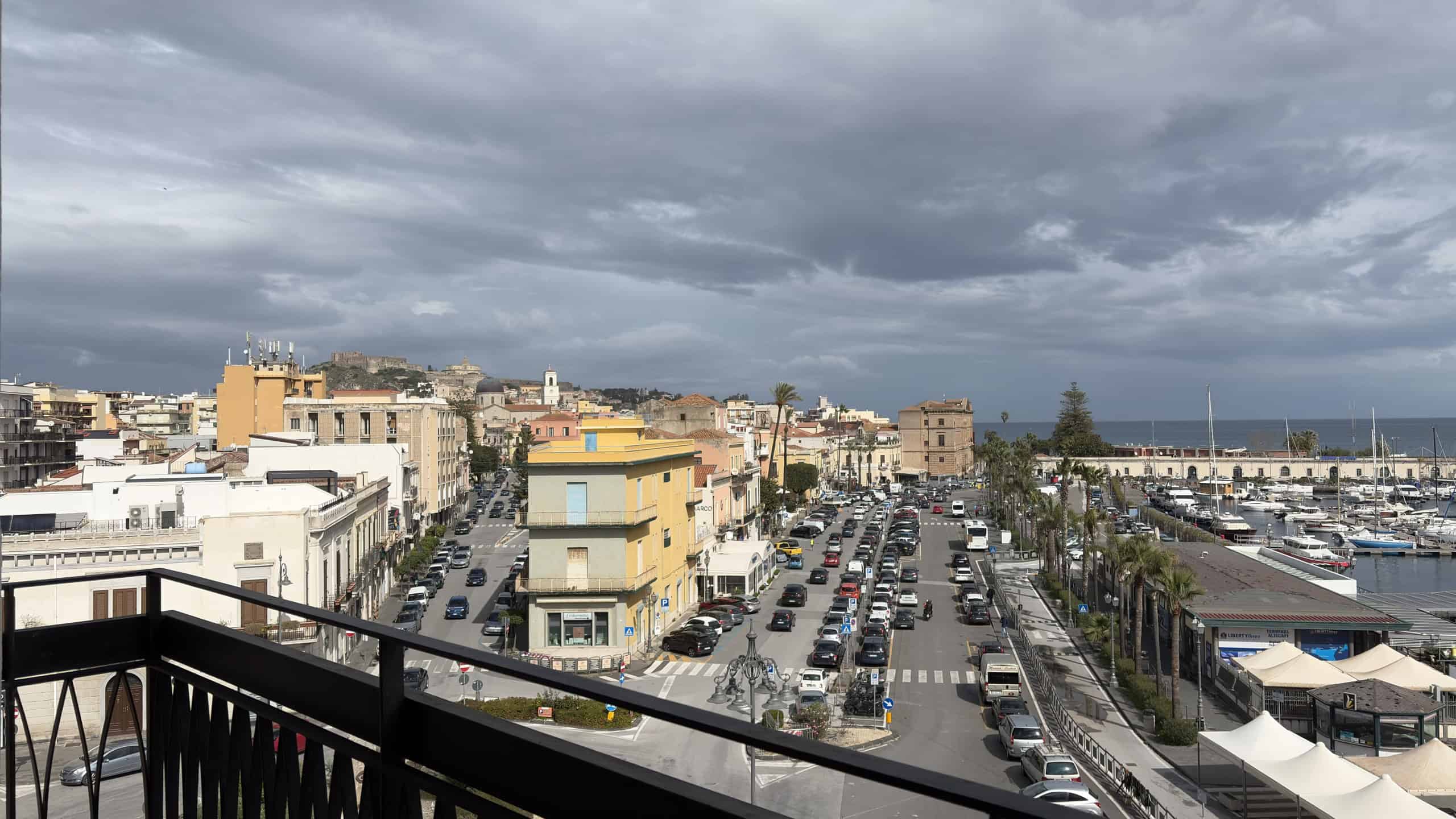 Vista panoramica del lungomare di una città costiera con edifici, parcheggi e marina, sotto un cielo nuvoloso, ideale per immobili e proprietà vicino al mare.