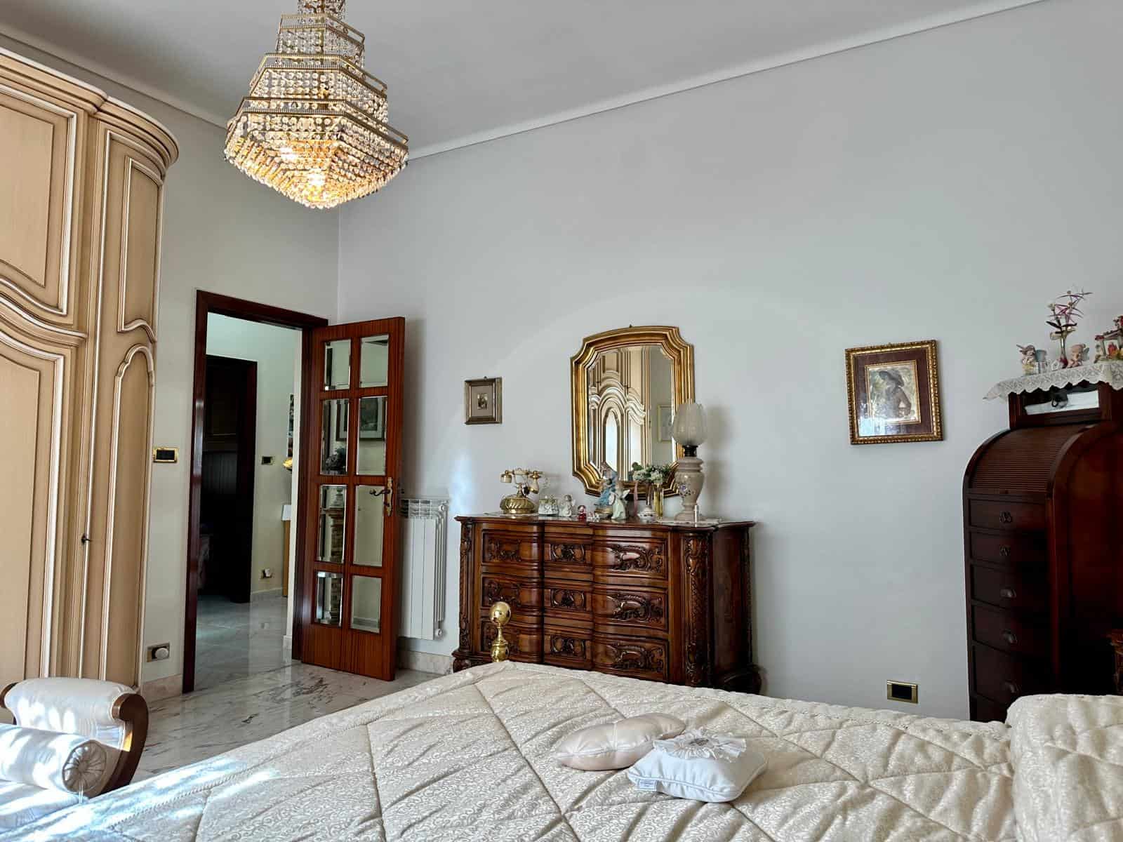 Elegante camera da letto con mobili d'epoca, specchio dorato e lampadario di cristallo, ambiente luminoso e accogliente, ideale per vivere in comfort e stile.