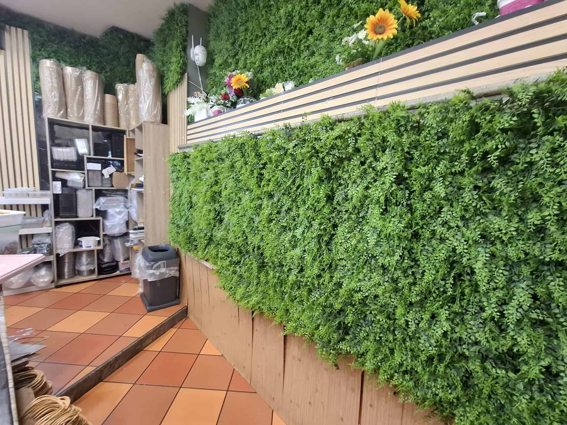 Pannello verde decorativo in un ambiente interno con piante e fiori colorati, ideale per arredi moderni e sostenibili.