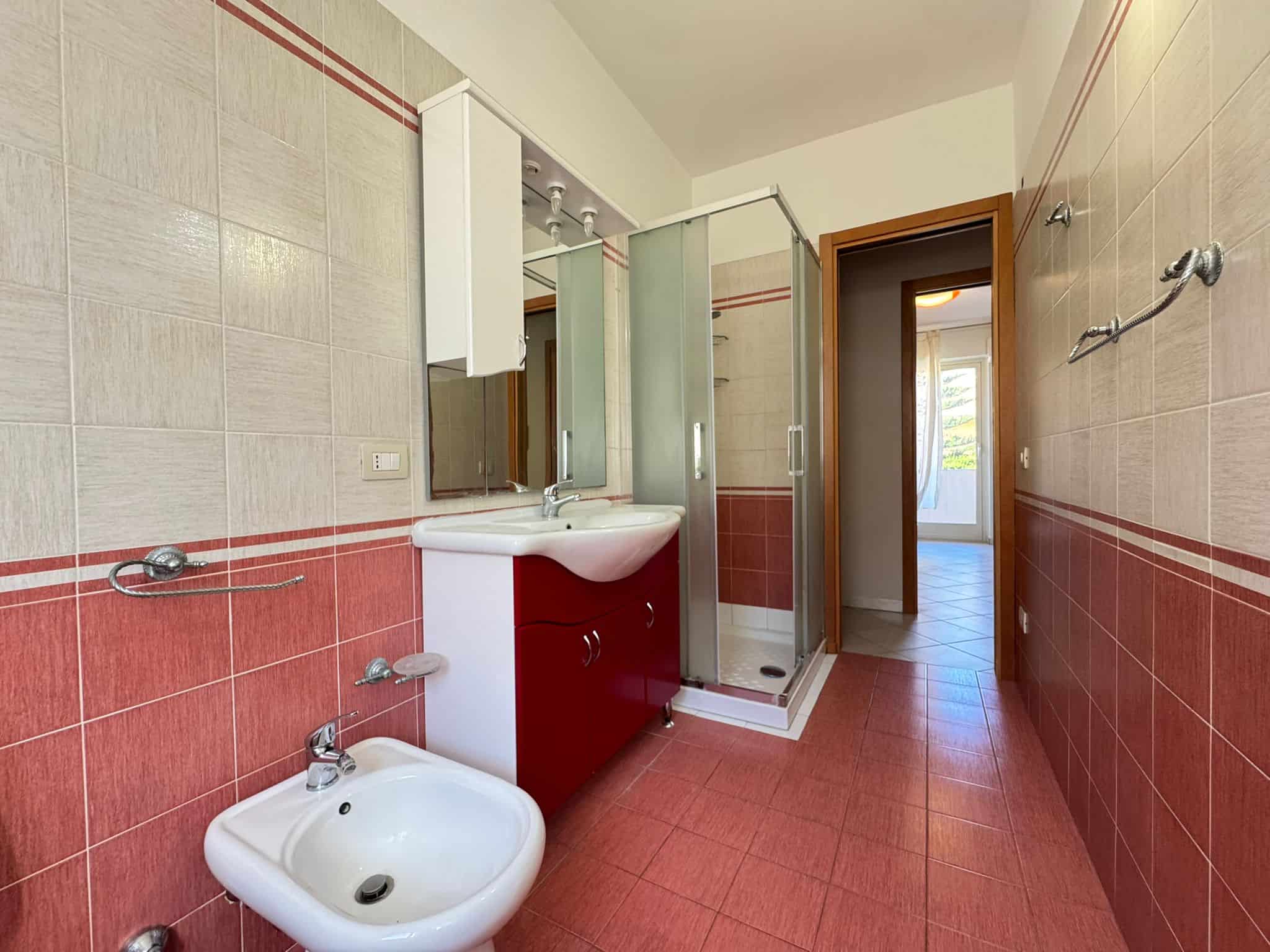 Ampia stanza da bagno con lavabo, doccia e bidet, rivestita con piastrelle beige e rosse, luminosa e spaziosa, ideale per il comfort quotidiano e il benessere.