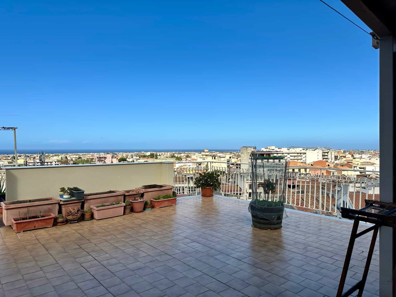 Vasto terrazzo con vista panoramica sulla città e il mare, arredato con piante in vaso e spazio per relax e socializzazione, ideale per vivere all'aperto in un ambiente luminoso e arioso.