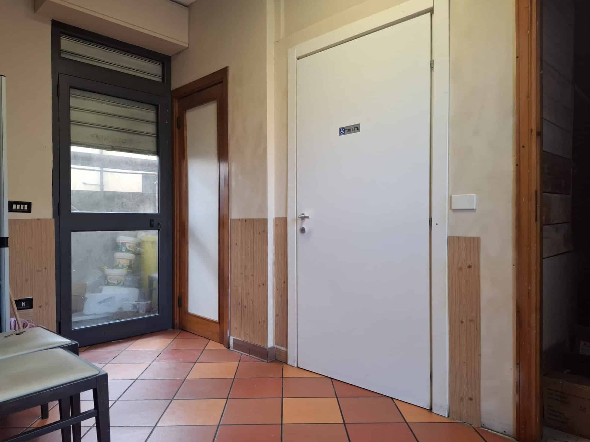 Porte d'ingresso e ingresso di un appartamento con pareti beige e pavimento in piastrelle di ceramica arancioni.