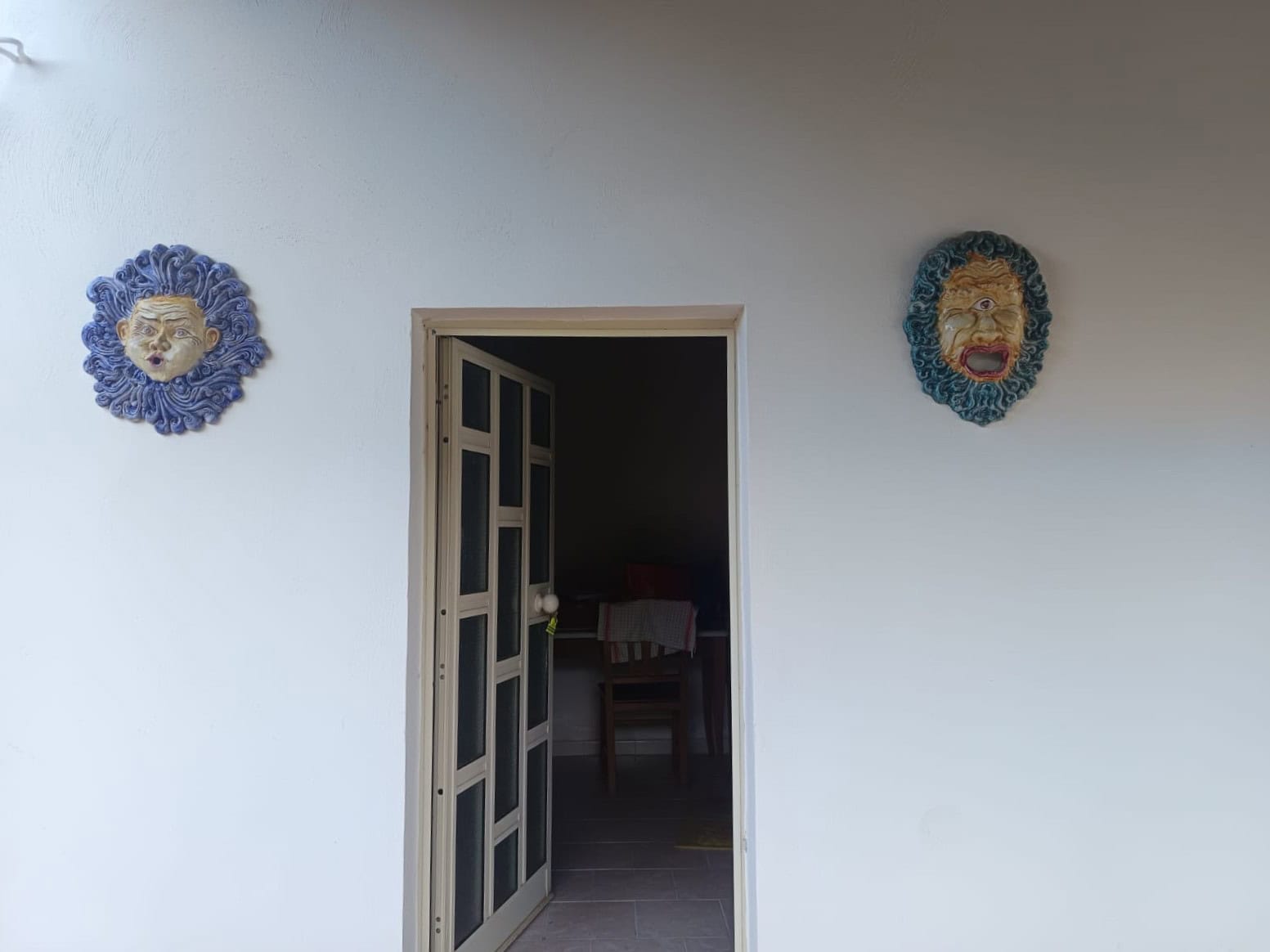 Maschere in ceramica colorata appese su parete bianca, decorazione artistica per interni di casa moderna.