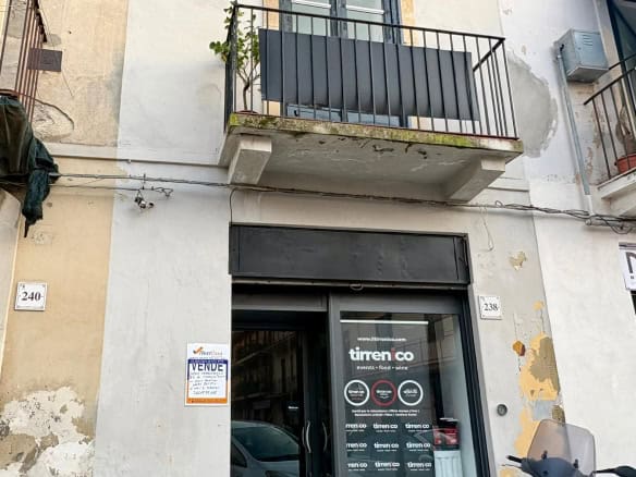 Balcone di un appartamento con porta finestra e ringhiera in metallo, situato in un edificio urbano con pareti in pietra e segni di usura, in zona residenziale di città.
