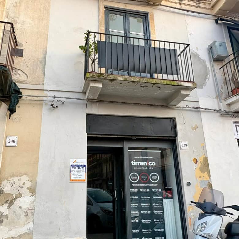 Balcone di un appartamento con porta finestra e ringhiera in metallo, situato in un edificio urbano con pareti in pietra e segni di usura, in zona residenziale di città.