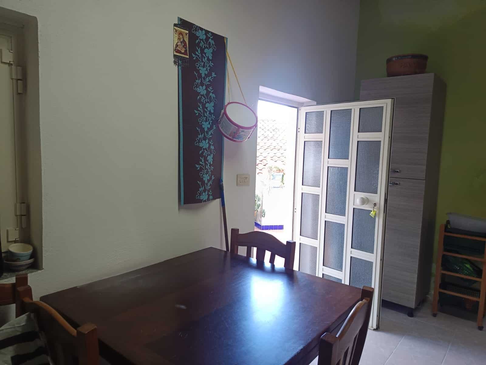 Lavagna e armadio in una stanza luminosa con tavolo in legno, sedie e decorazioni colorate, ambiente accogliente e funzionale.