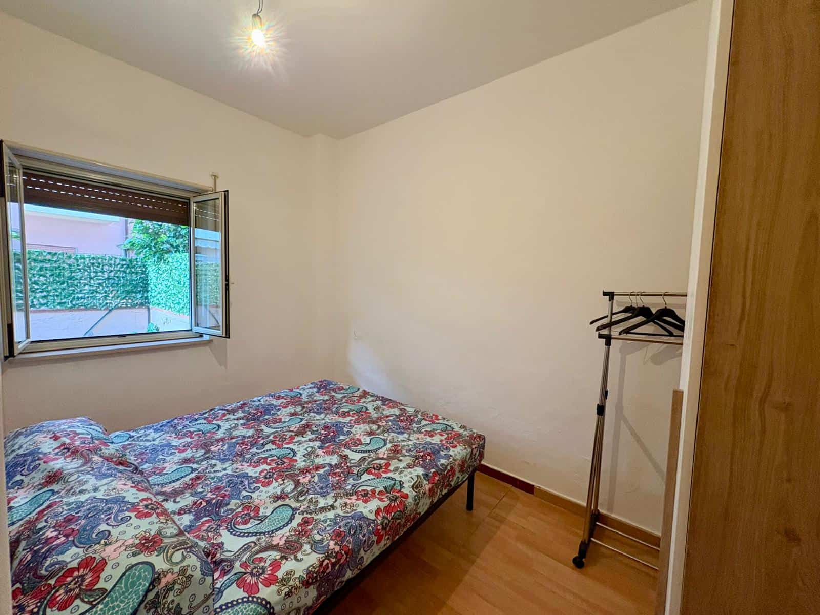 Camere da letto con pareti bianche, pavimento in legno e finestra che permette l'ingresso di luce naturale, arredate con un letto matrimoniale e un appendiabiti, ideale per ambienti residenziali.