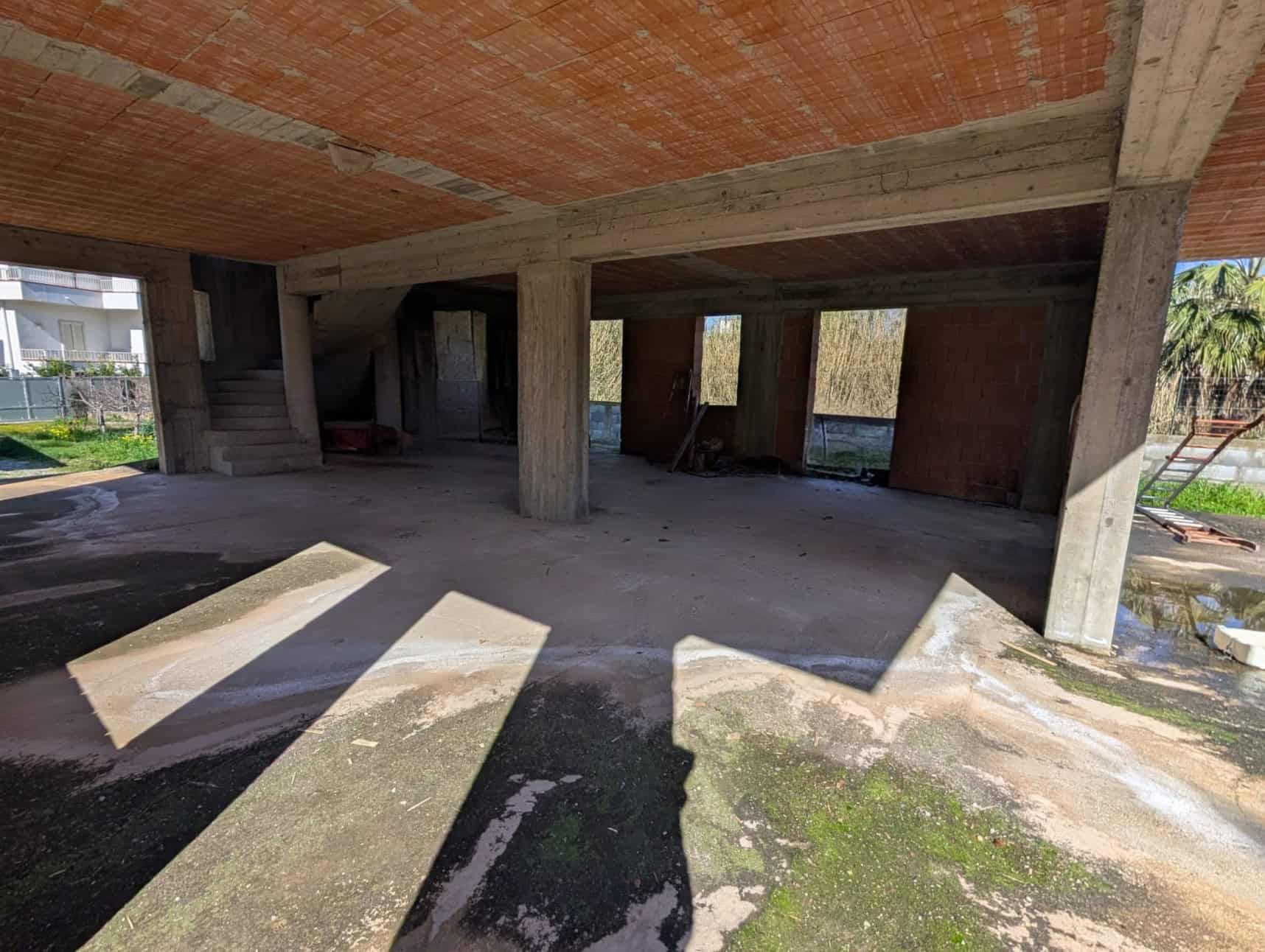 Pilastra di cemento e struttura in costruzione di un edificio residenziale, con pareti e soffitto in fase di completamento, illuminato dalla luce naturale e con un'area esterna circostante in fase di.