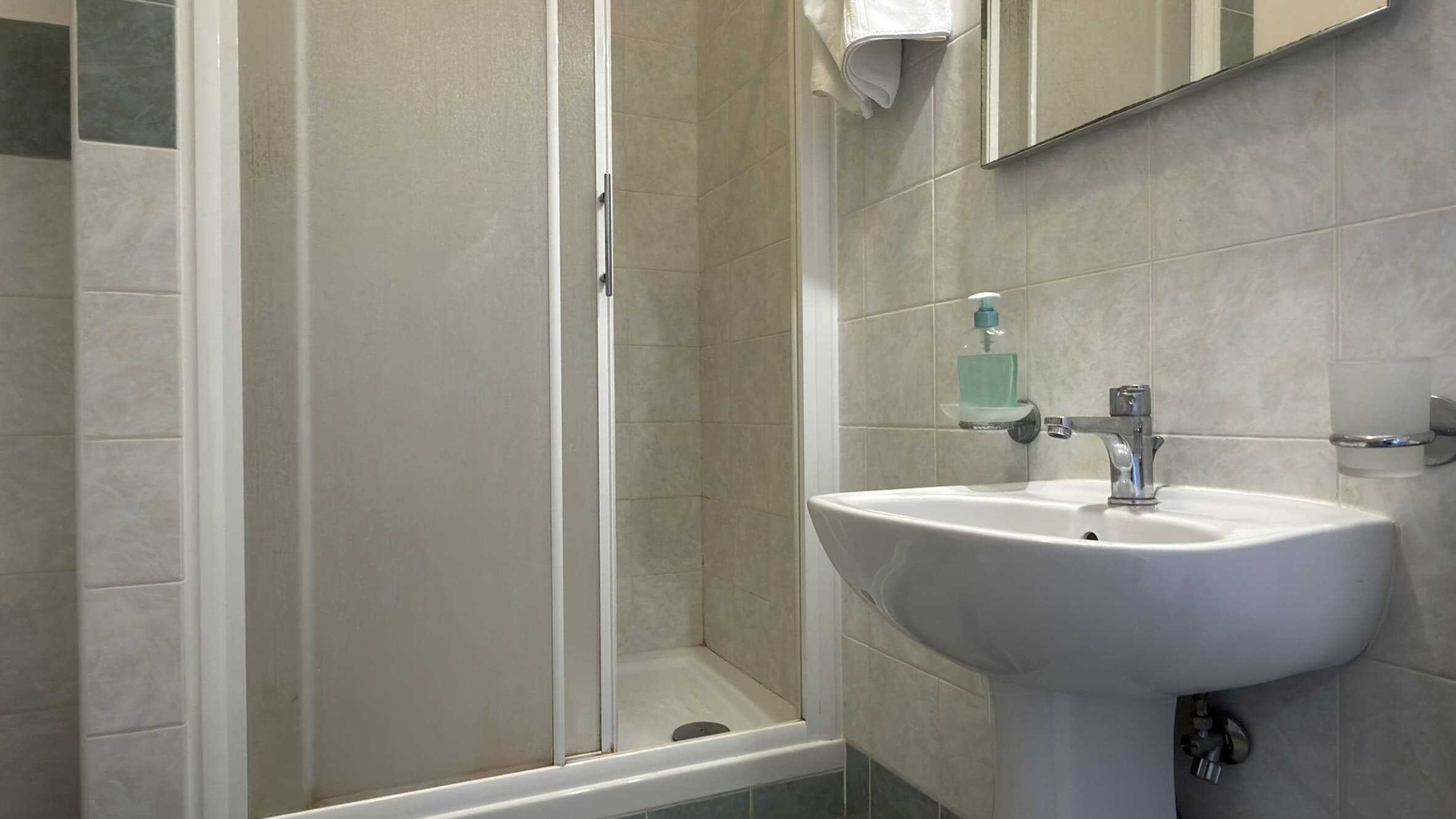 Lavabo e doccia in un bagno moderno con piastrelle beige, sanitari funzionali e spazio ottimizzato per il comfort quotidiano. Ideale per appartamenti e case di design.