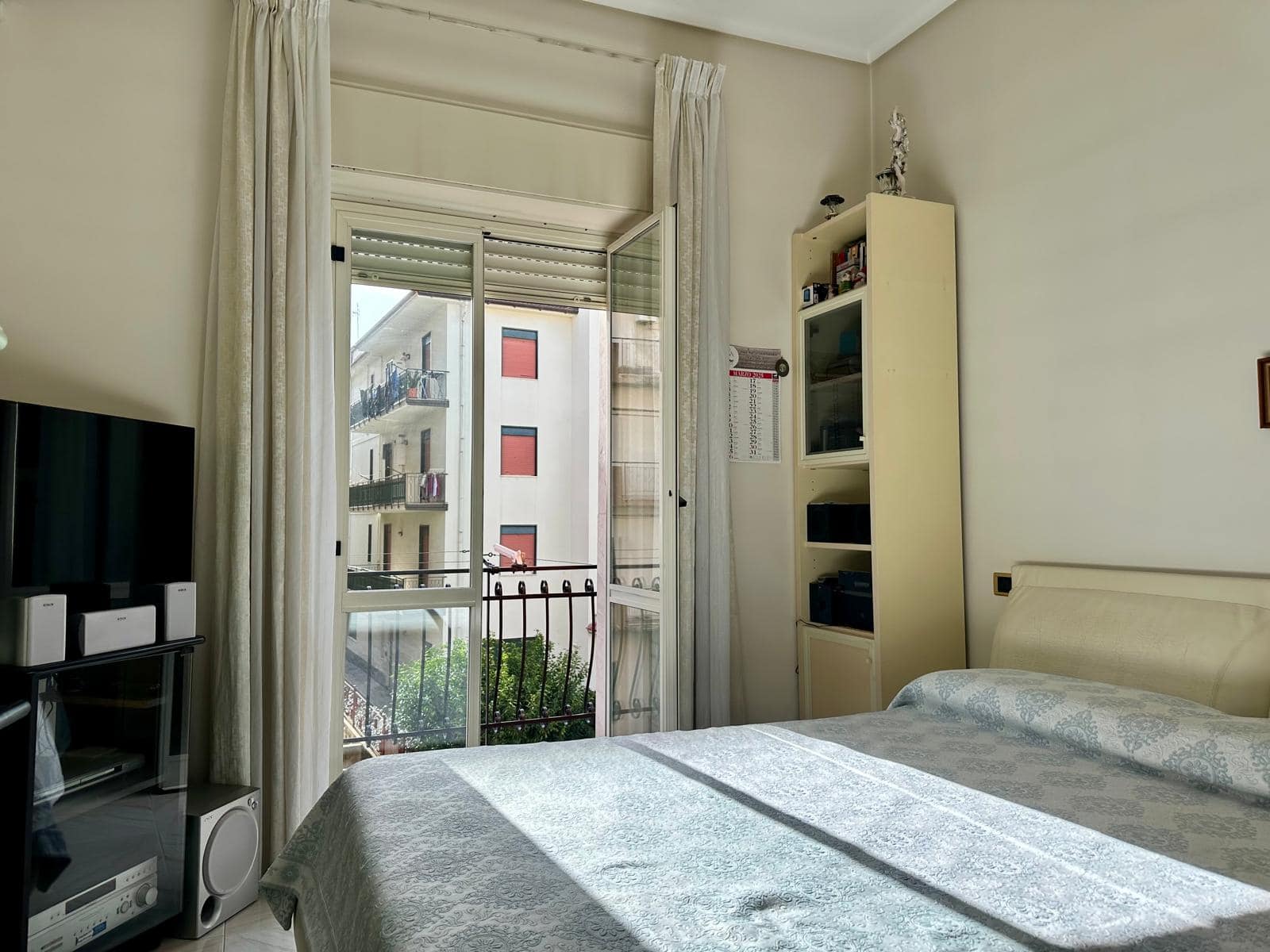 Vetro scorrevole con balcone e vista su edifici residenziali, stanza da letto luminosa e accogliente con arredi moderni, ideale per appartamenti in centro città.