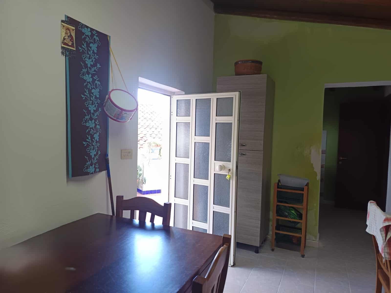 Pannello decorativo con motivi floreali blu e rosa, lampada a sospensione, porta finestra che permette l'ingresso di luce naturale, arredi in stile semplice e funzionale, ambiente luminoso e accoglien.
