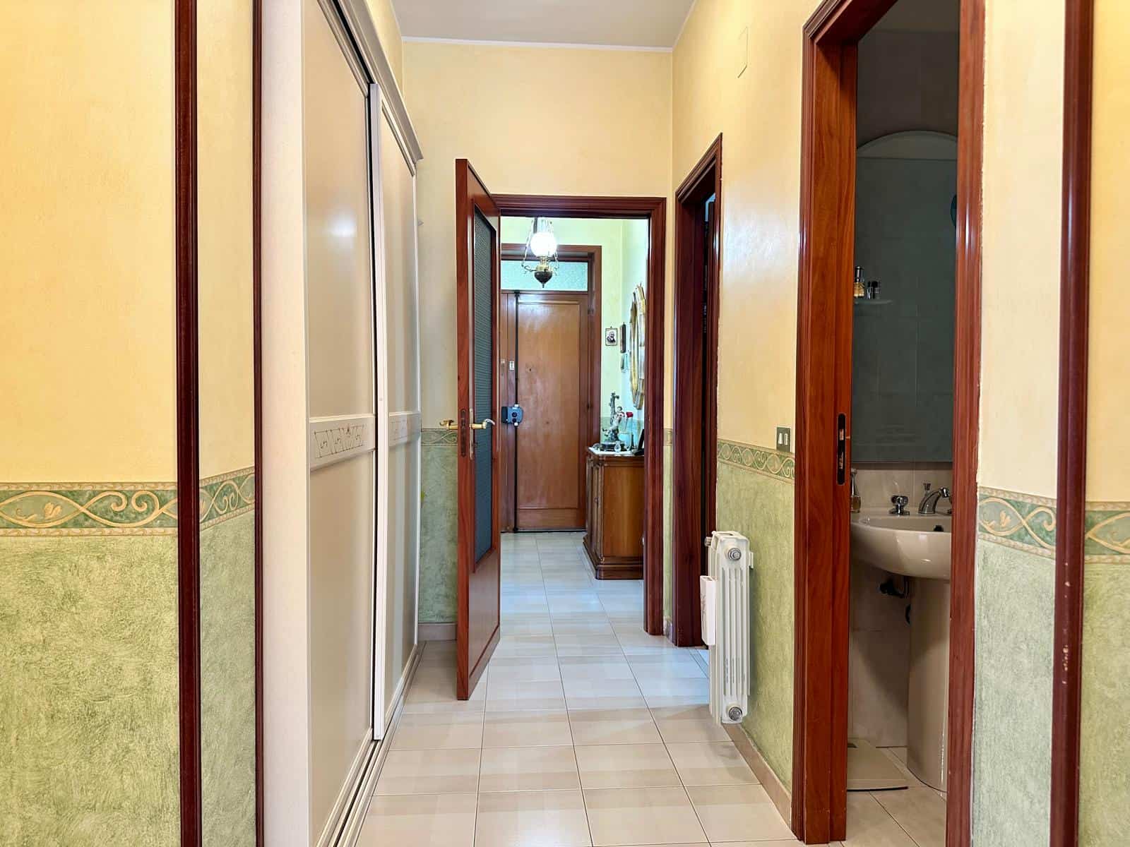 Corridoio interno di una casa con pareti gialle e verde, porte in legno e un radiatore visibile, ambiente luminoso e accogliente.