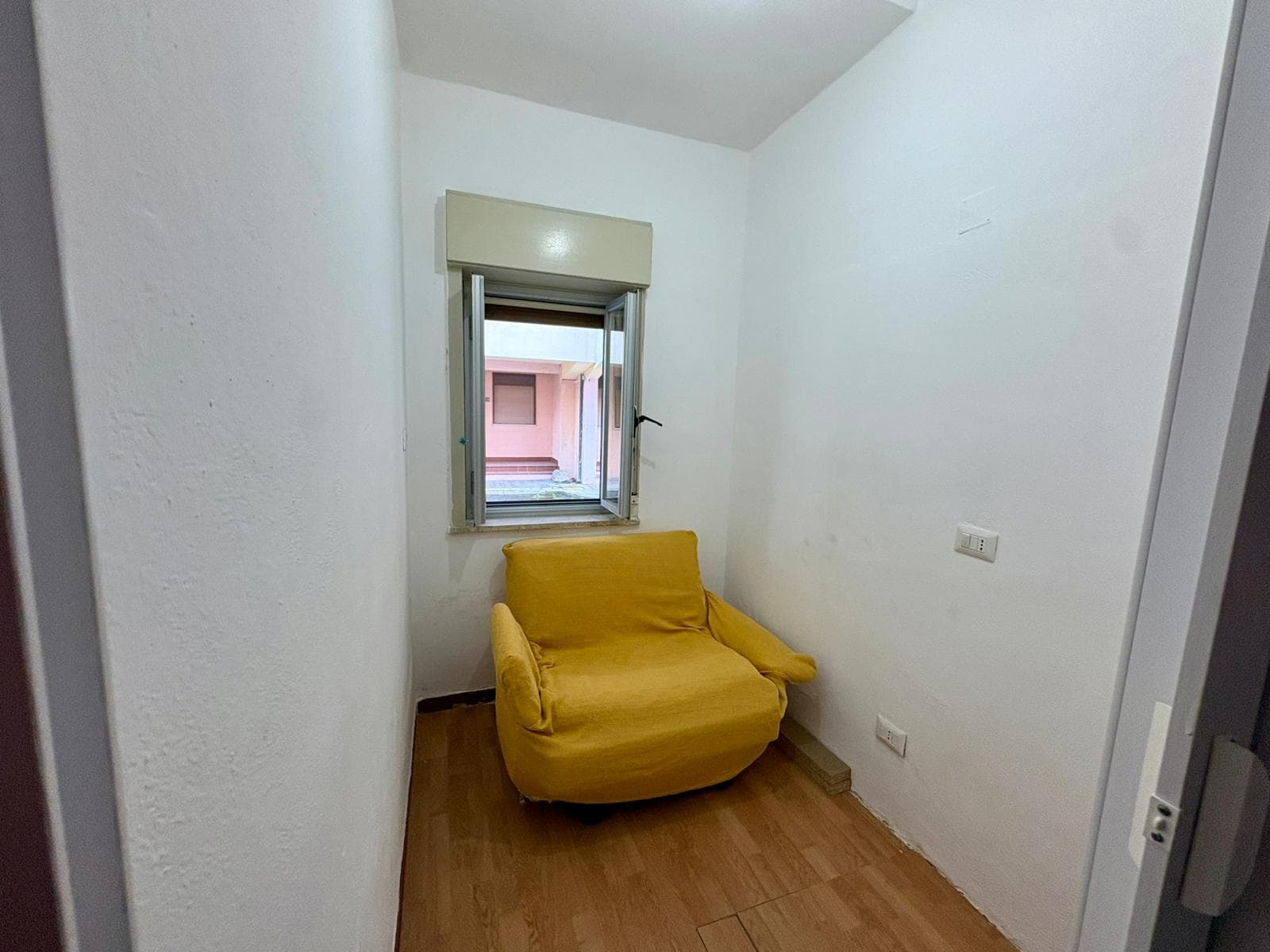 Sedia gialla in una stanza piccola con pareti bianche e finestra, ambiente semplice e minimalista.