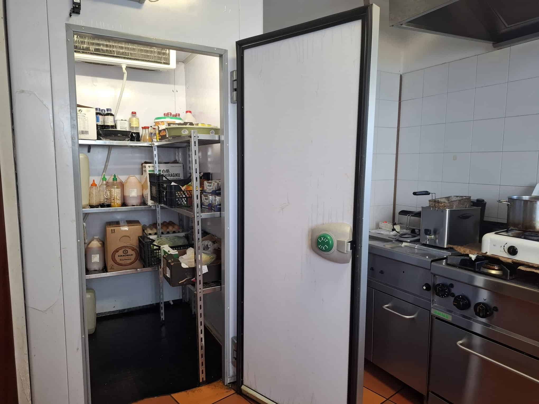 Ripostiglio con scaffalature metalliche e dispense alimentari in cucina professionale.