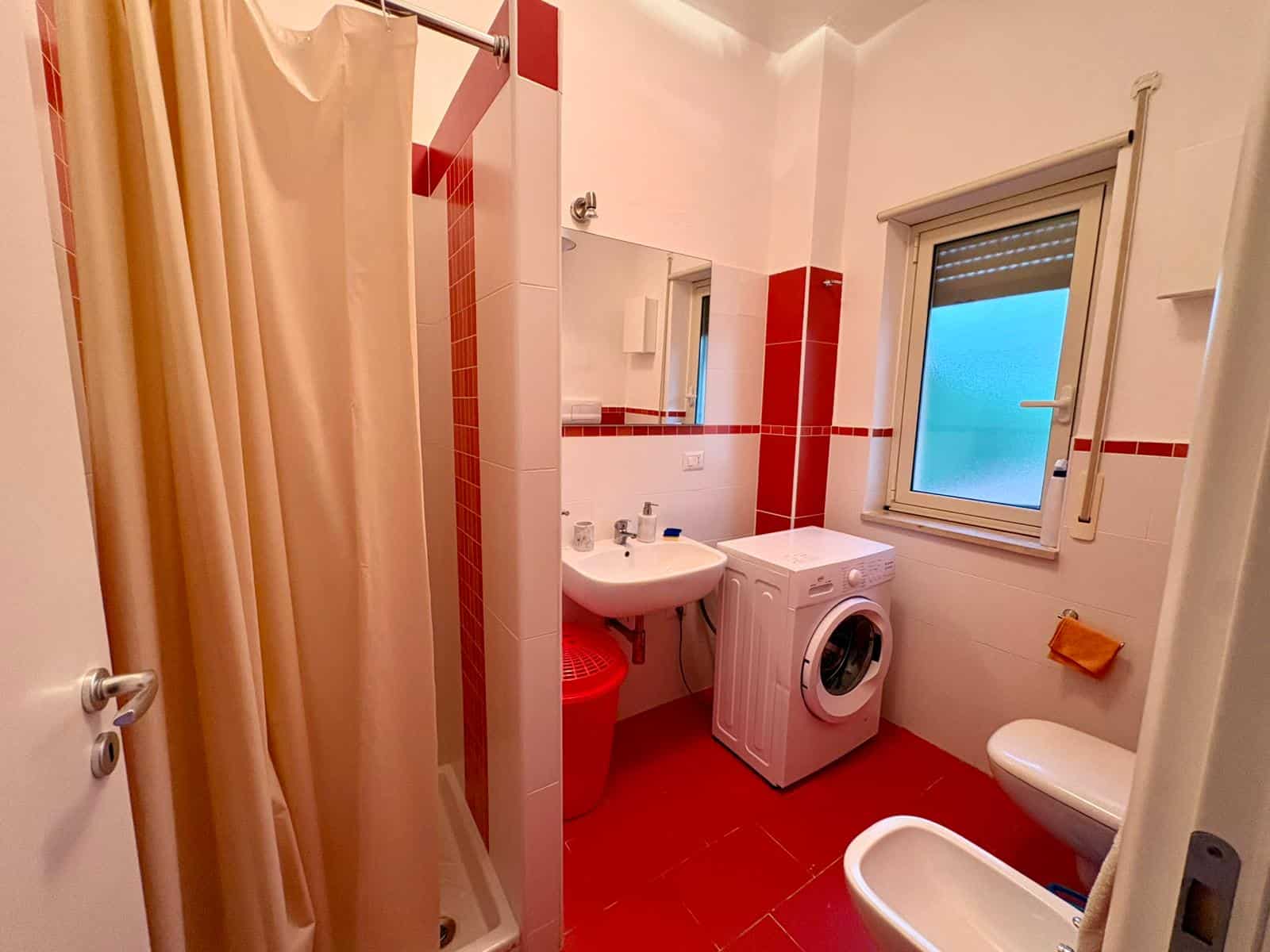 Lavatrice e bagno con piastrelle rosse e bianco, finestra con vista sul cielo, spazio funzionale e moderno, ideale per appartamenti o case in Italia.