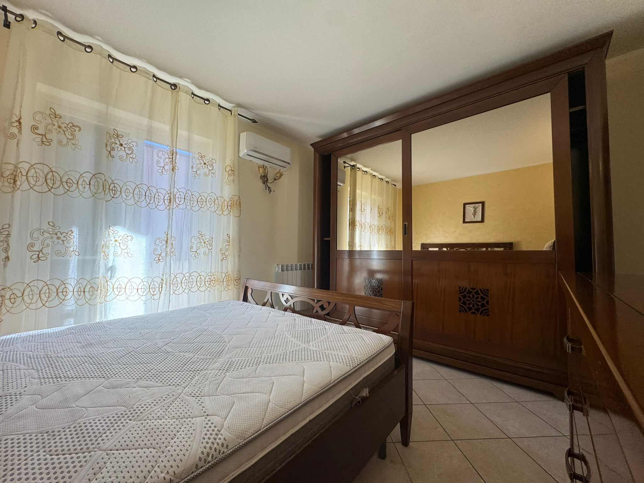 Il letto matrimoniale in una camera da letto luminosa con tende leggere e aria condizionata, ideale per soggiorni confortevoli e rilassanti.