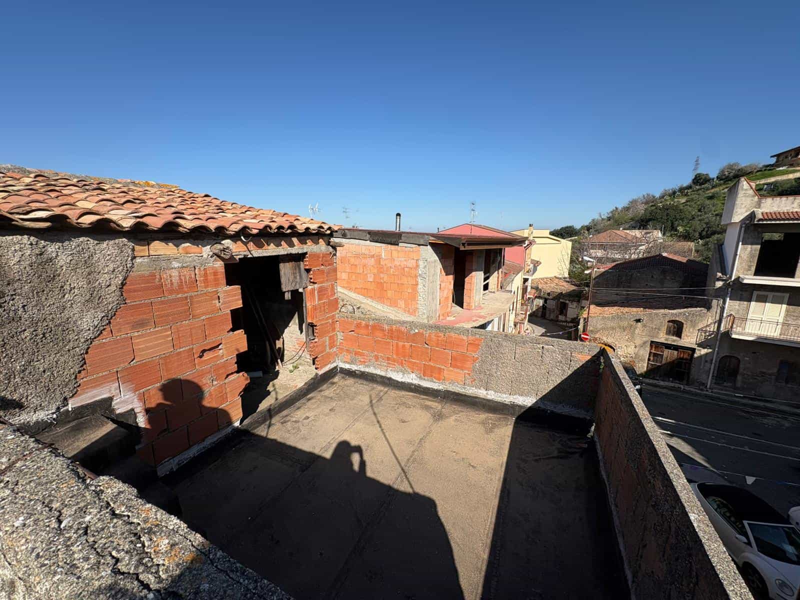 Il tetto di un edificio residenziale in fase di ristrutturazione con mattoni rossi e strutture in cemento, vista panoramica sul cielo azzurro e sui tetti circostanti.