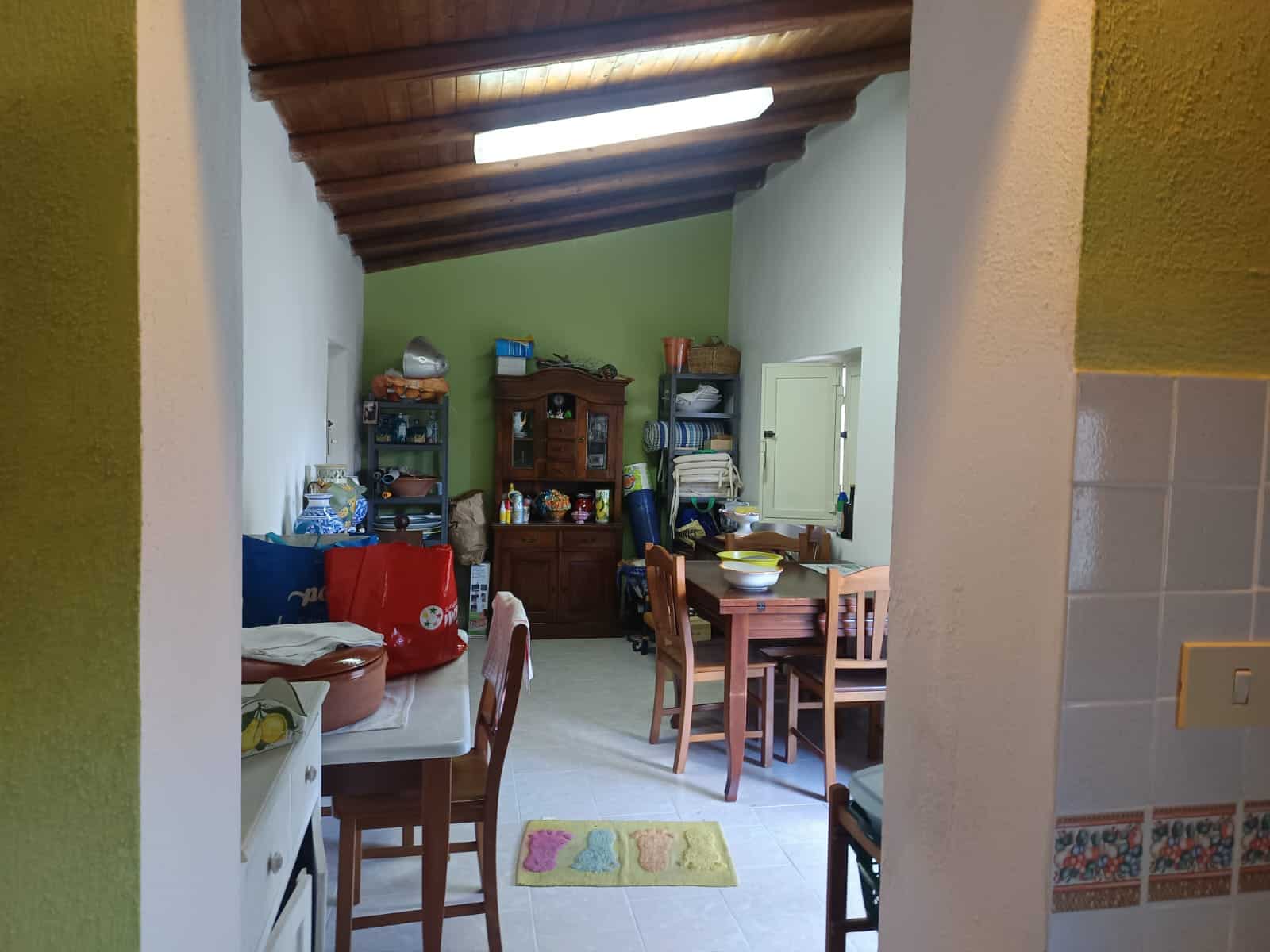 Interno di una cucina accogliente con mobili in legno, pareti verdi e soffitto in legno, con tavolo e sedie, ideale per vivere momenti conviviali in casa.