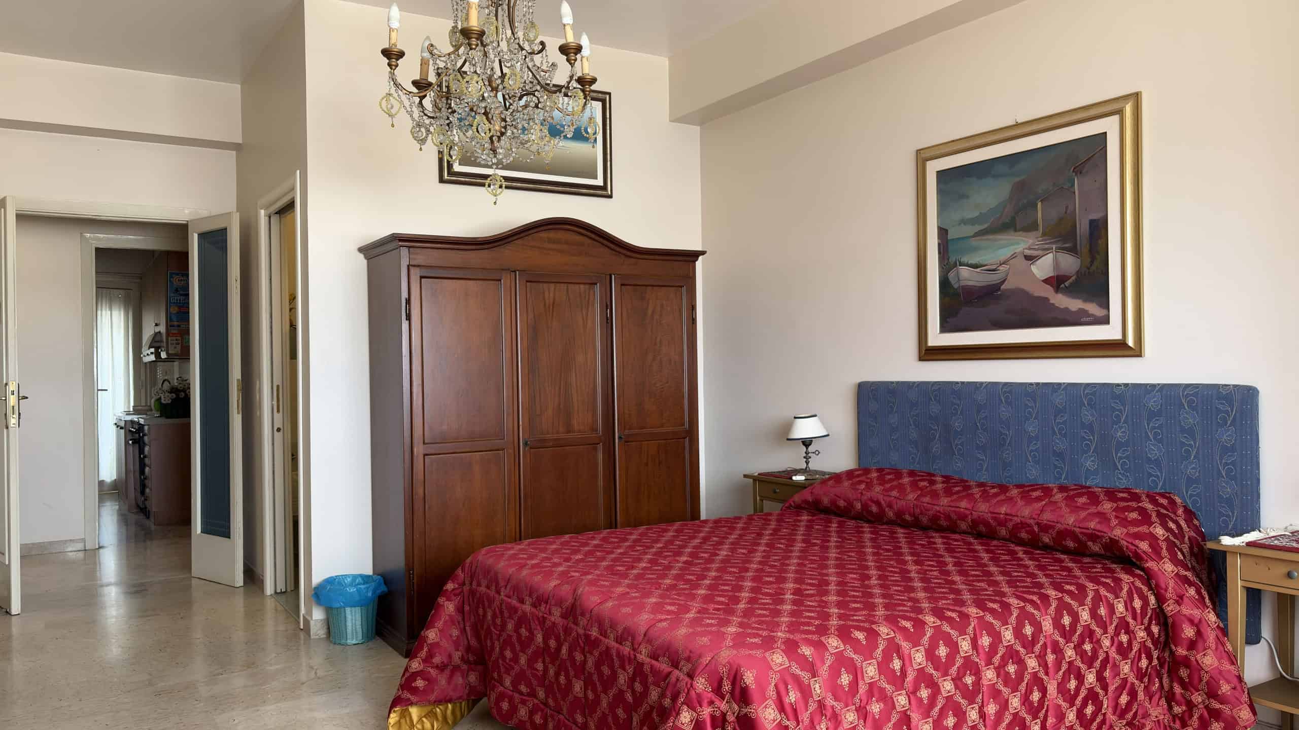 Elegante camera da letto con letto matrimoniale, armadio in legno, lampada da comodino e quadro artistico, in un ambiente luminoso e accogliente, ideale per soggiorni confortevoli.