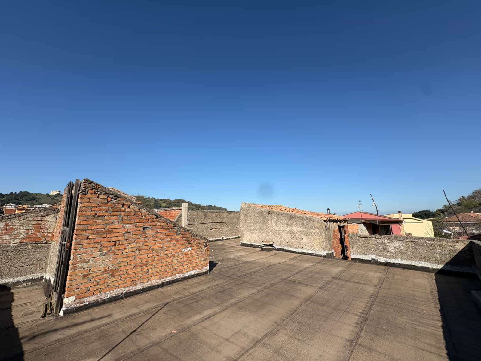 Aggiunta di un tetto di copertura in cemento e mattoni su un edificio residenziale con vista sul cielo azzurro e sul paesaggio urbano circostante.